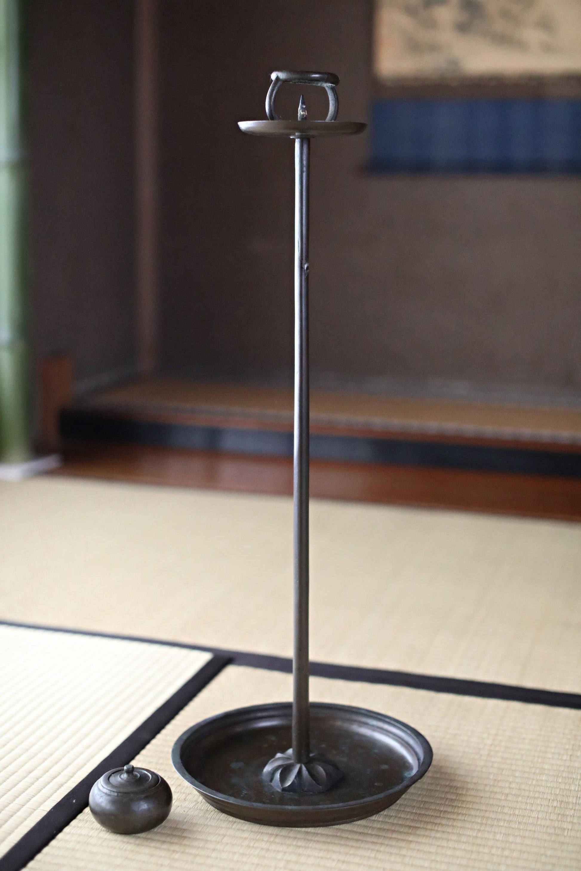 a black metal candle holder with a small black candle in it, placed on a woven mat.