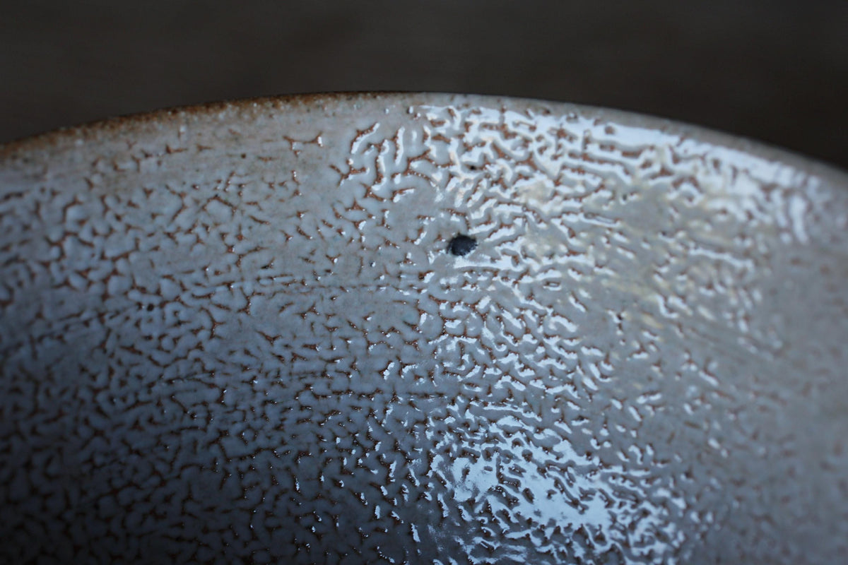 a close-up view of a textured ceramic bowl or dish with a small hole or puncture mark visible on its surface.