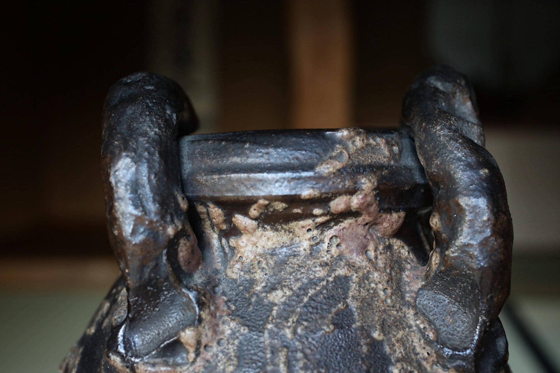 A close-up view of a dark, textured metal object, possibly a piece of pottery or a sculpture, with a rough, weathered appearance.