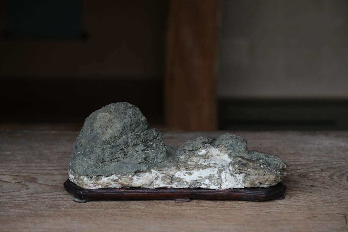 A large, gray rock sits on a wooden base, placed on a wooden surface.