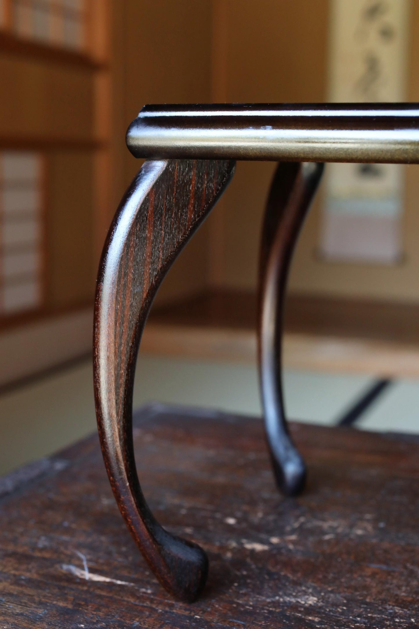 A close-up view of a wooden table leg with a curved, dark finish, situated on a wooden surface.