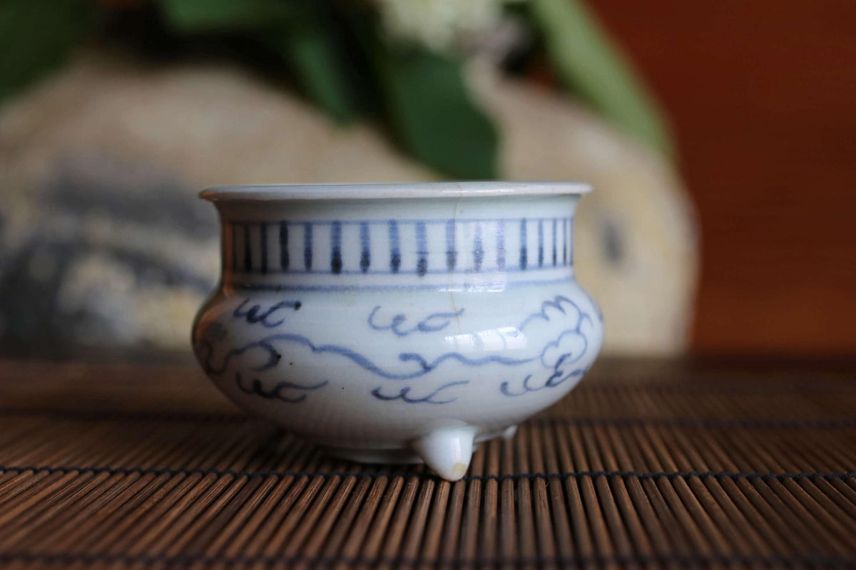 A white ceramic bowl with blue and black designs sits on a bamboo mat.