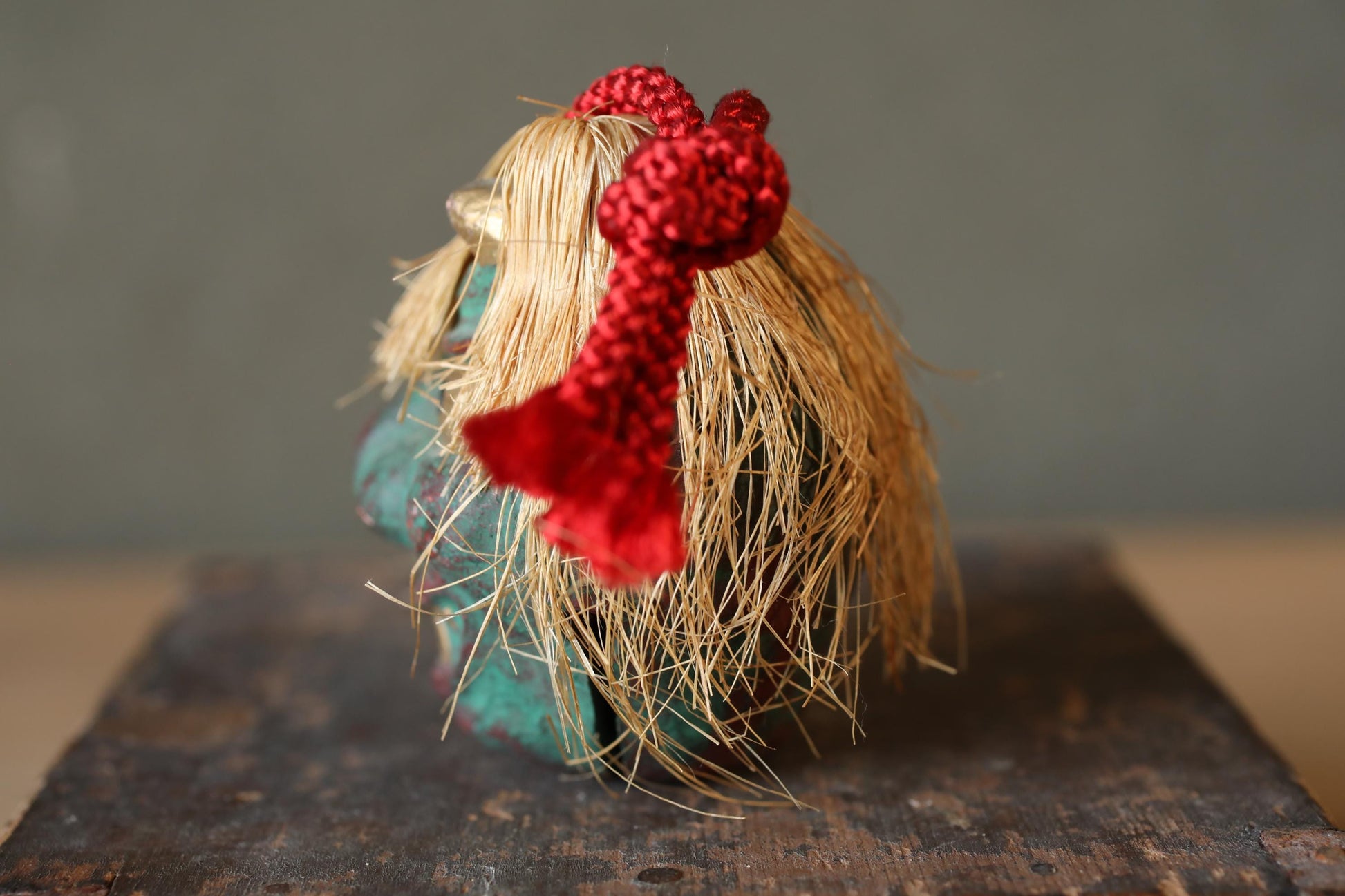 A small, intricately crafted figurine made of straw and painted in a vibrant green color, with a red ribbon tied around its head.