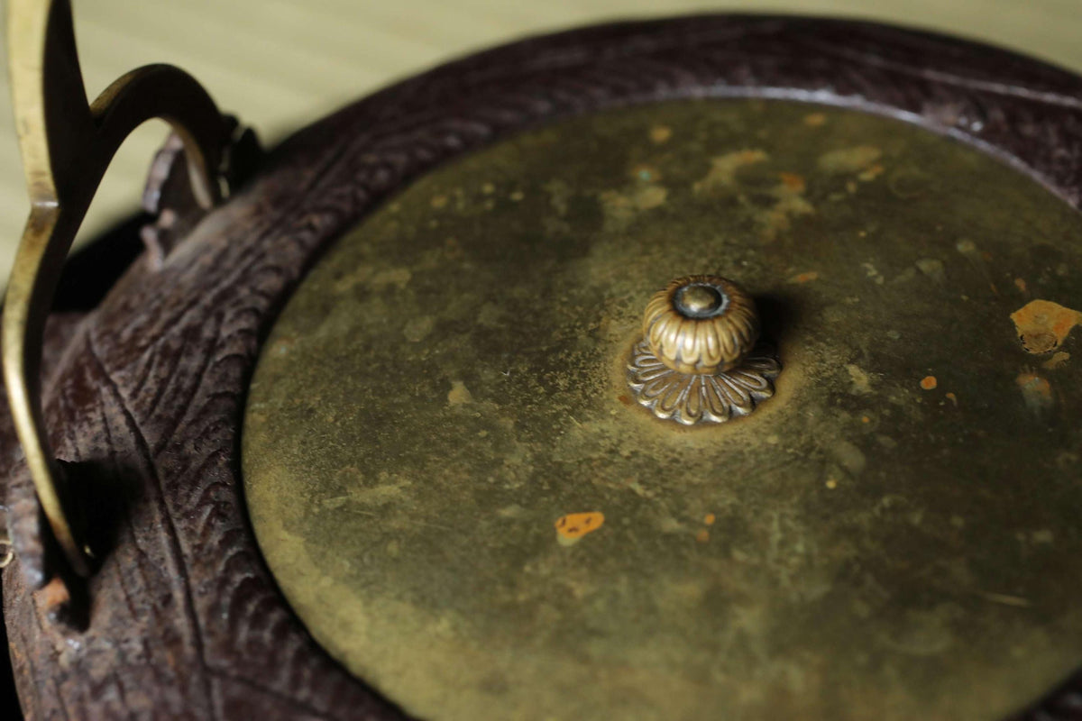 a close-up view of a brass-colored metal object, possibly a decorative piece or a container, with a small, ornate finial or knob on top.