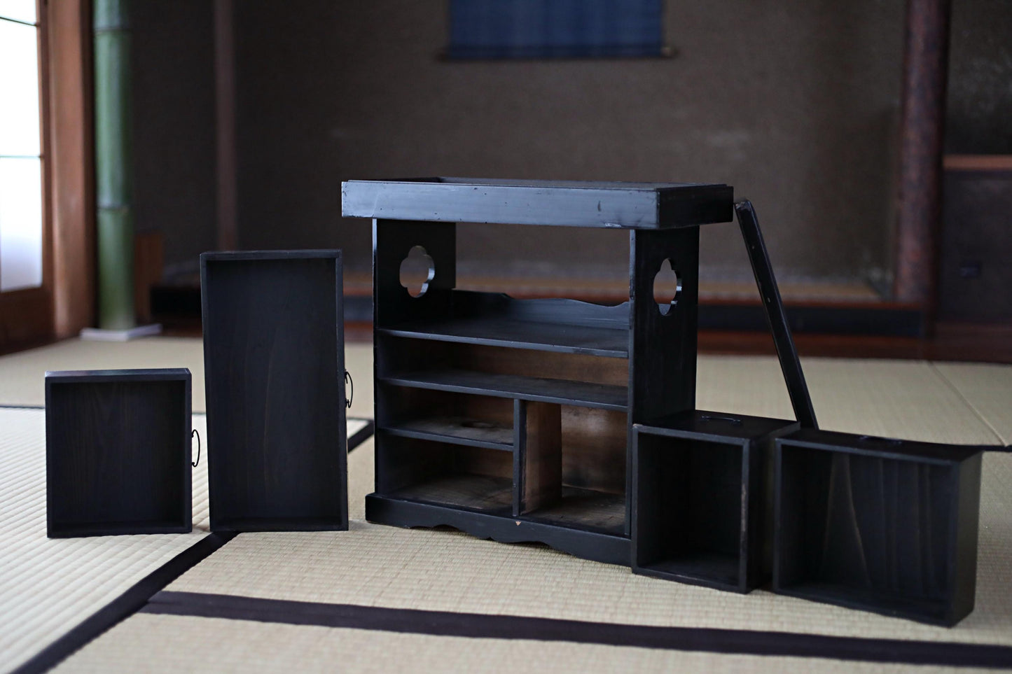 A wooden shelf with multiple compartments and drawers, placed on a tatami mat in a room with a wooden wall and a window.