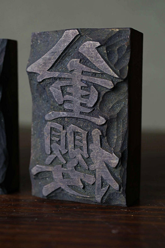 a dark wooden block with an intricate carved design, including a symbol or text that appears to be in a foreign language.