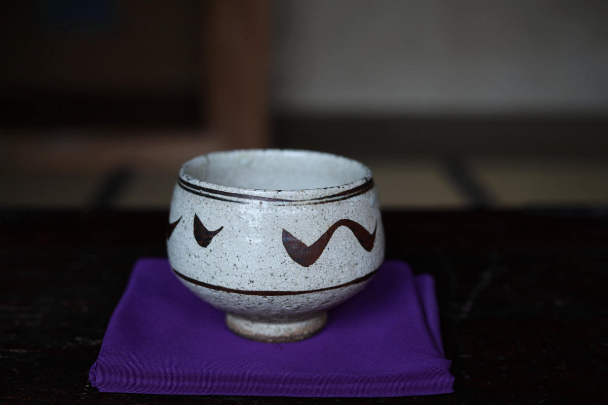 A white ceramic bowl with a black wavy pattern sits on a purple cloth on a dark surface.