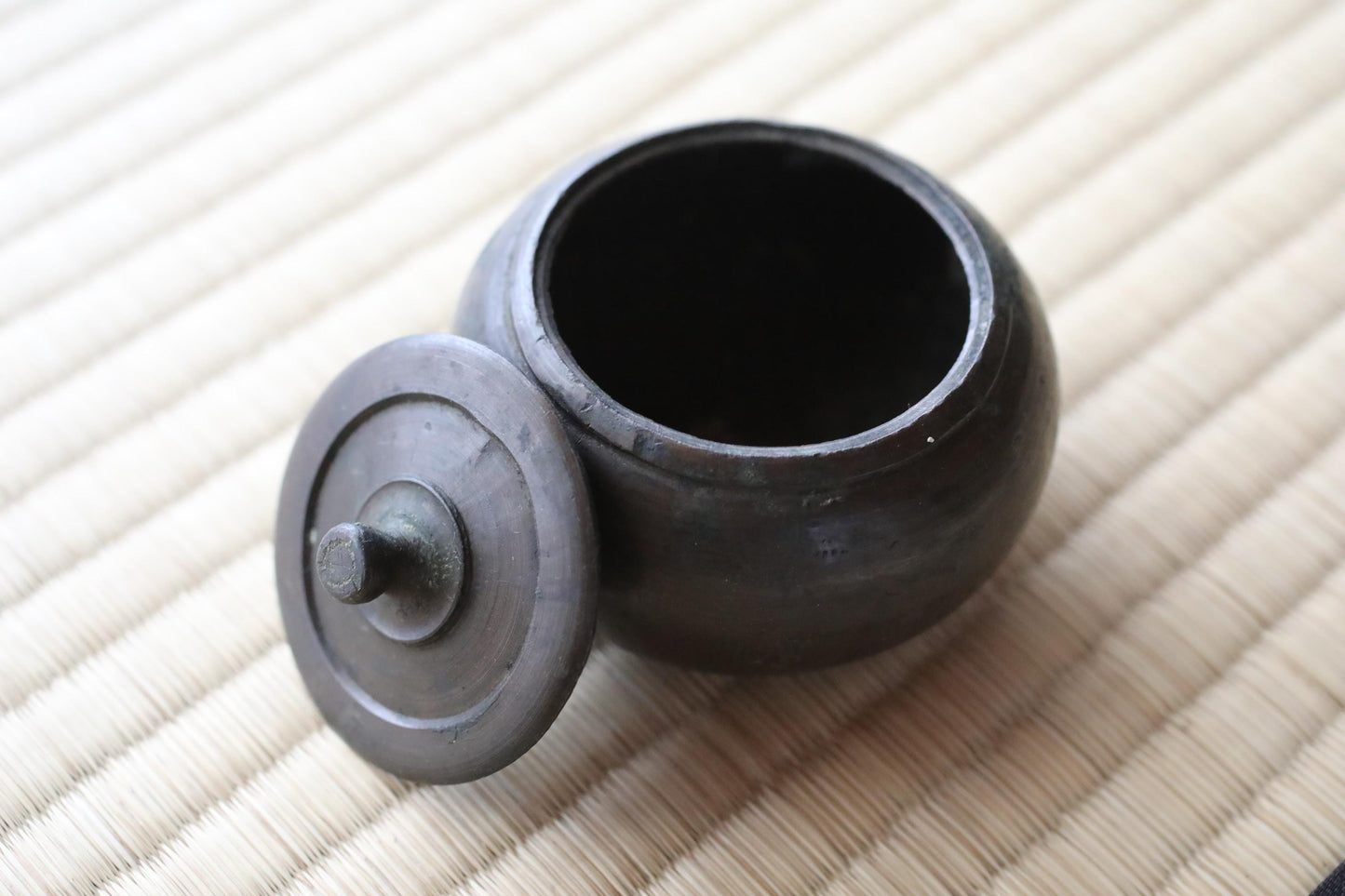 A black metal bowl with a lid sits on a woven mat.