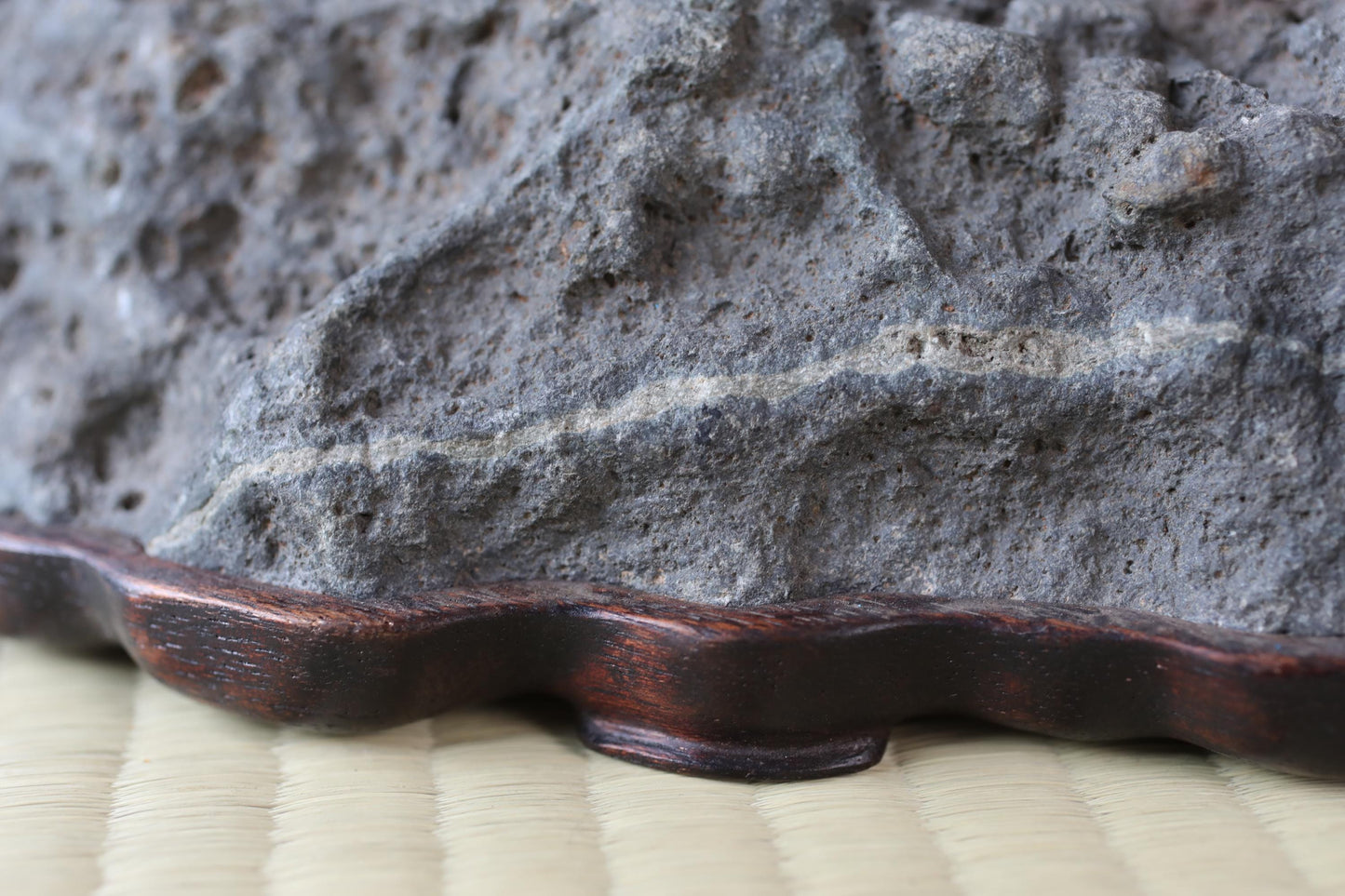 a close-up view of a rock or stone surface, with a wooden base or stand placed on a woven mat or mat-like material.
