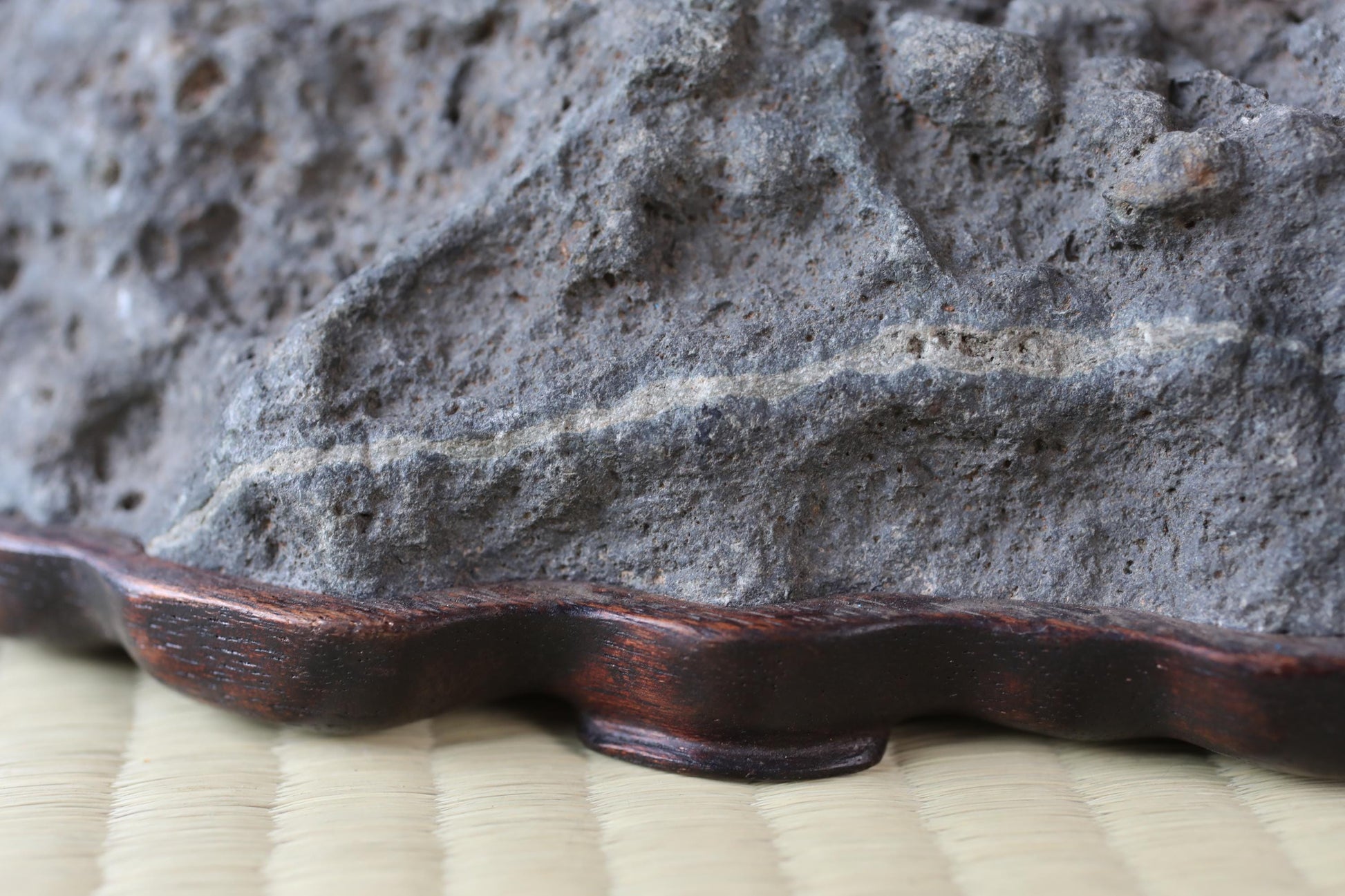 a close-up view of a rock or stone surface, with a wooden base or stand placed on a woven mat or mat-like material.