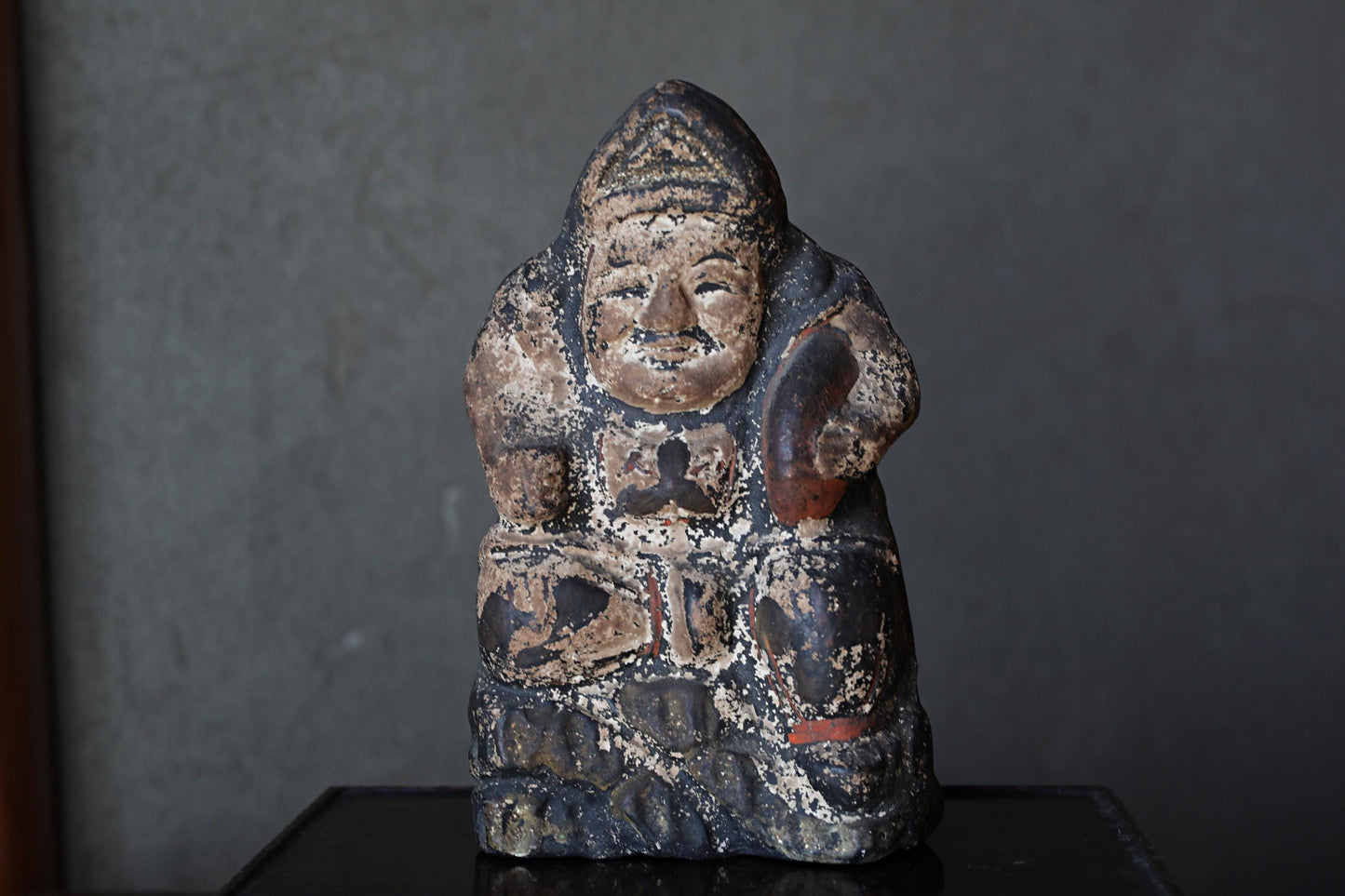 An old, weathered statue of a seated figure, possibly a deity or religious figure, with a dark, textured appearance.