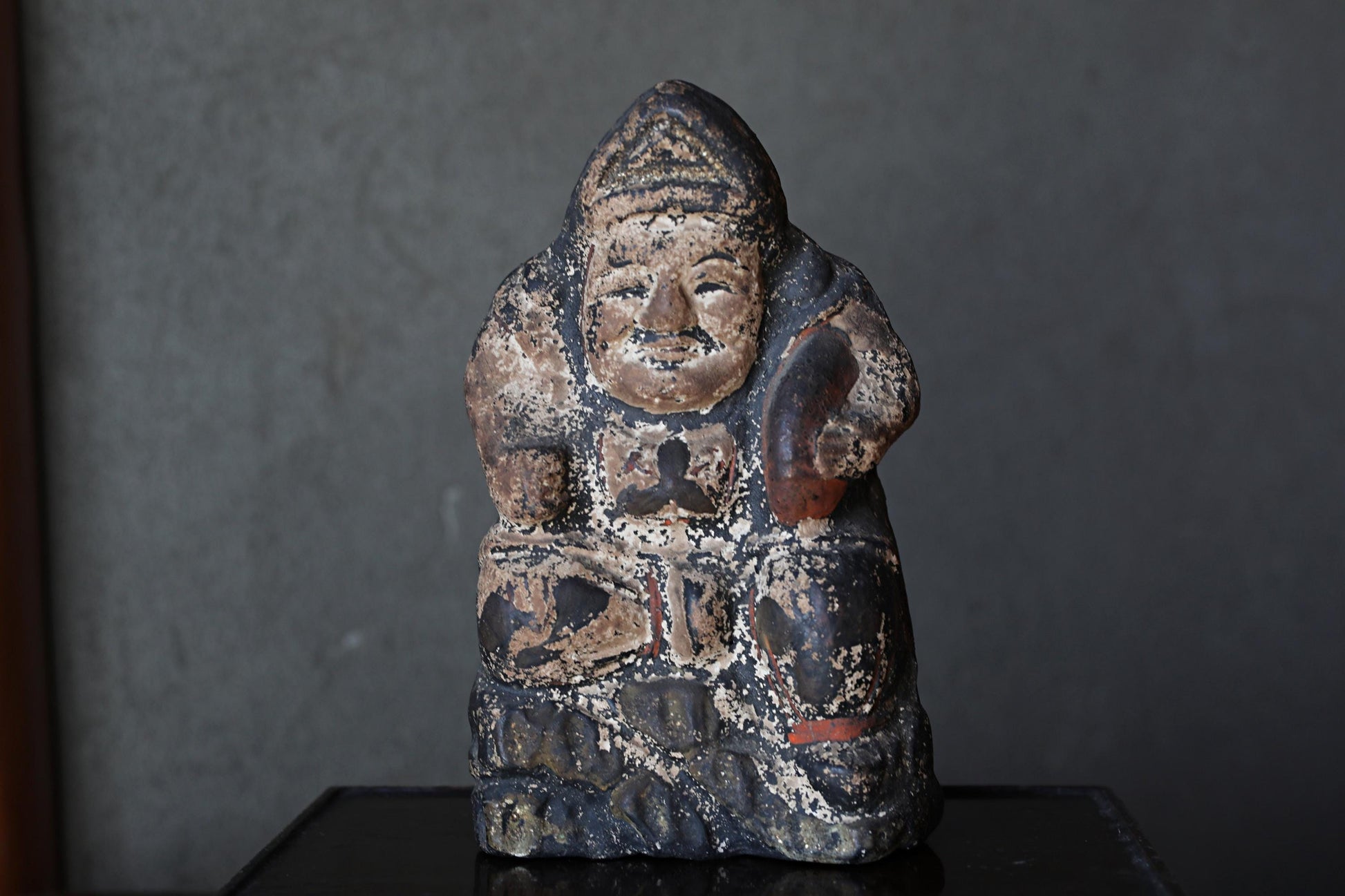 An old, weathered statue of a seated figure, possibly a deity or religious figure, with a dark, textured appearance.
