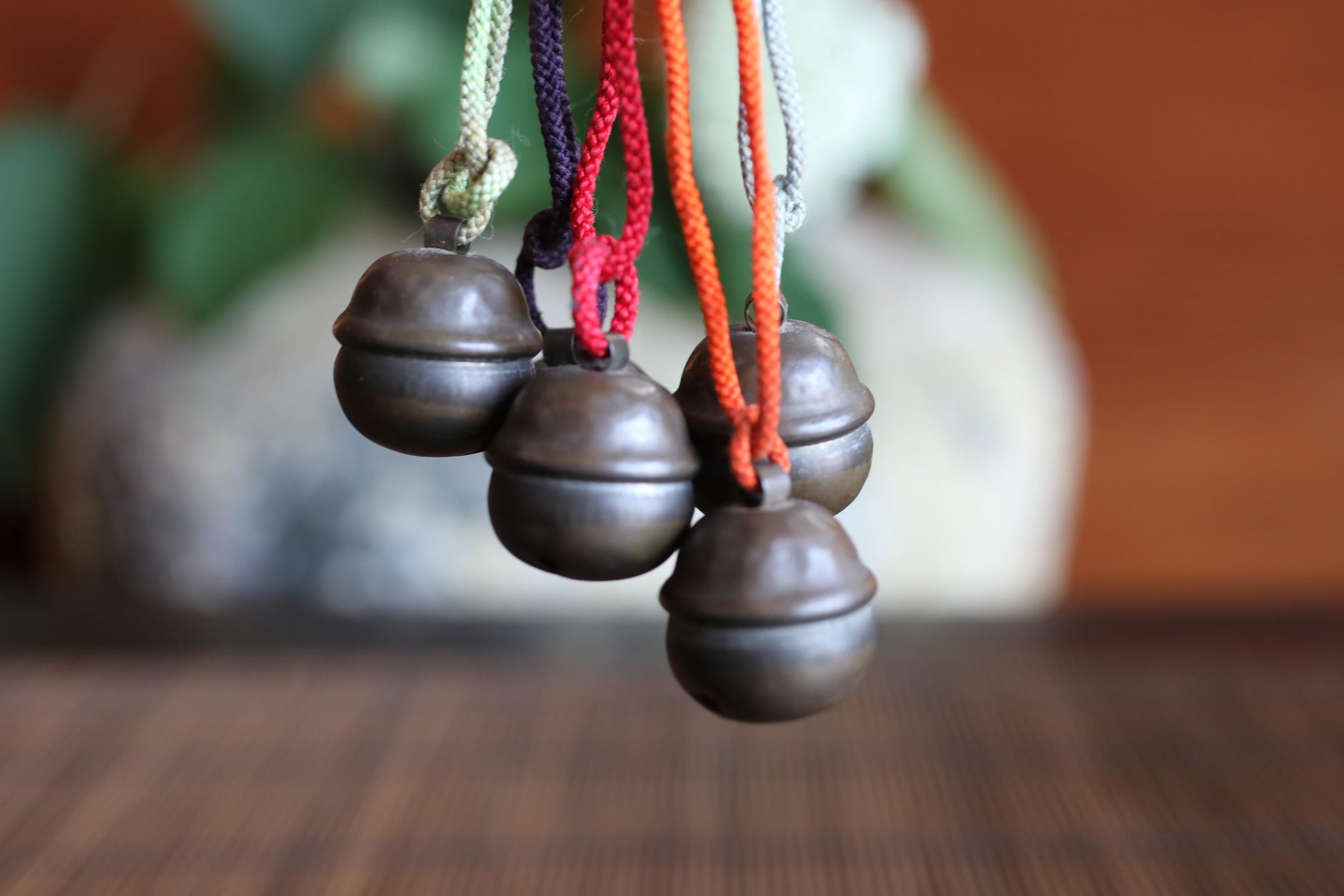 a close-up view of four metal bells hanging from strings, with a blurred background that appears to be a plant or similar natural element.