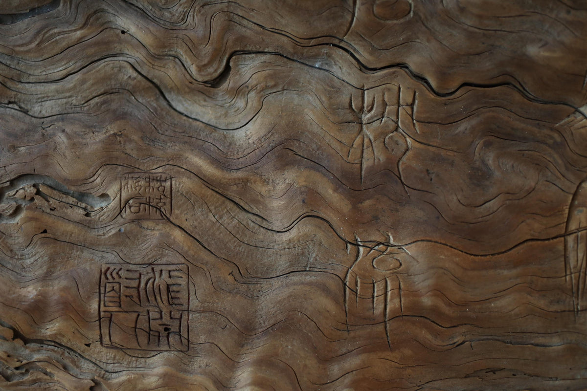 a close-up view of a wooden surface with intricate patterns and designs, including carved symbols and text.