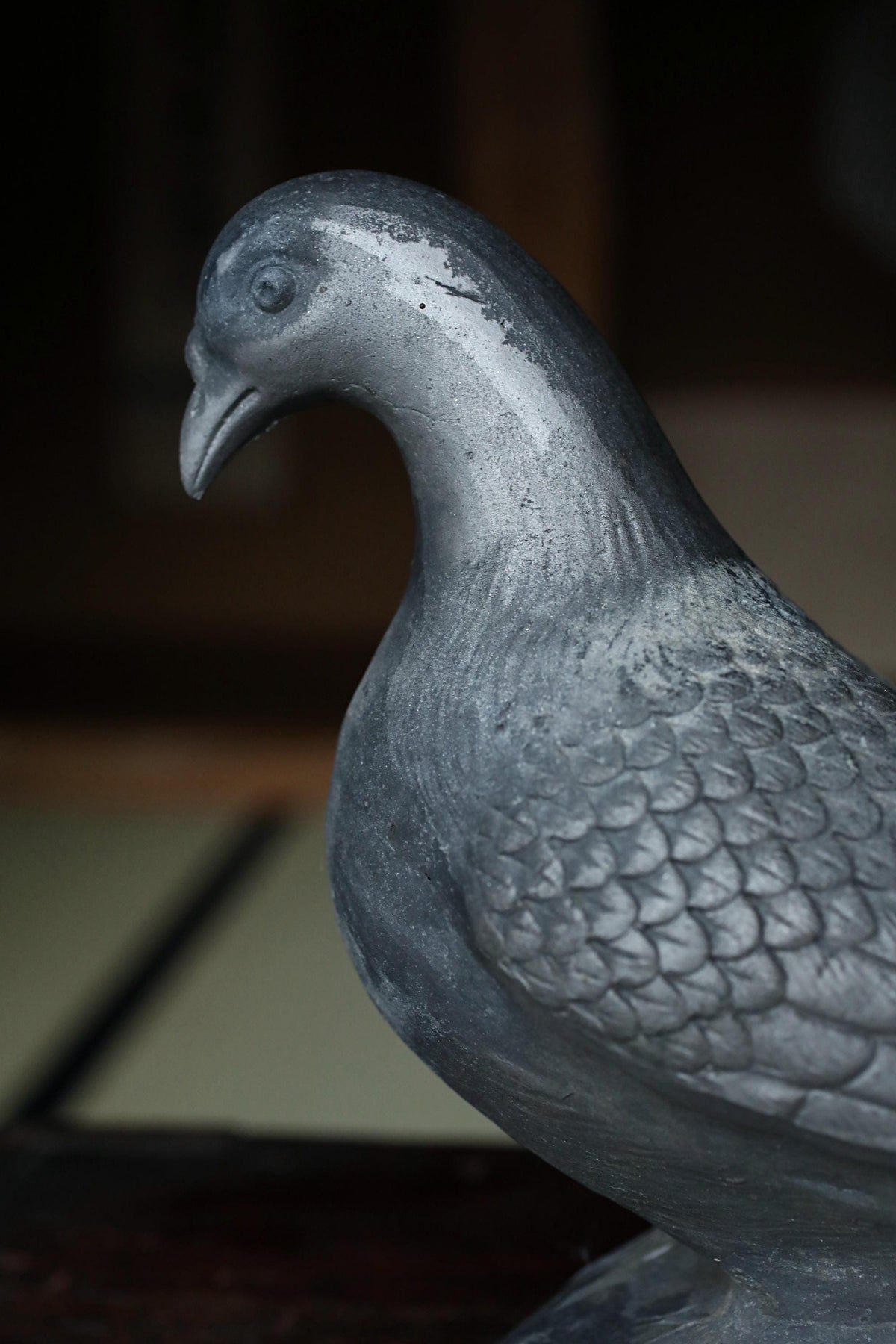 A close-up view of a metal bird statue, possibly a pigeon, with a textured, shiny appearance.
