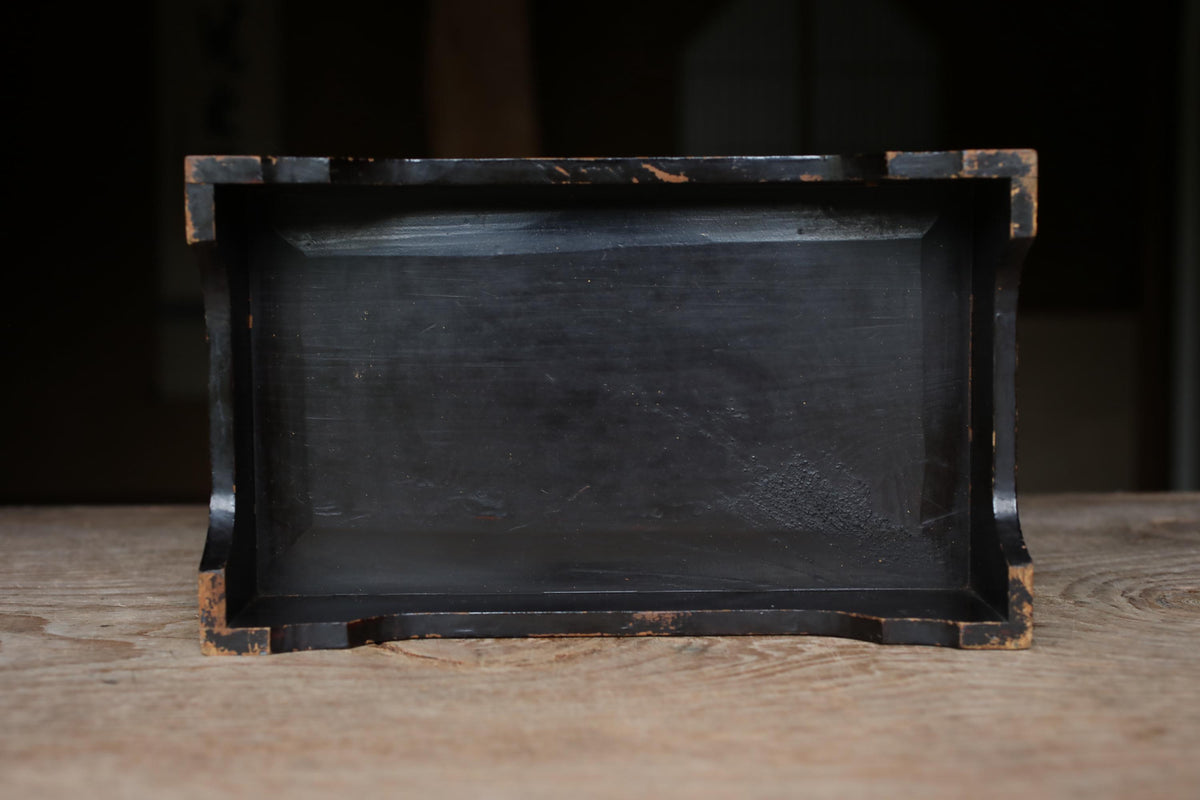 A black, rectangular box with a weathered, distressed appearance sits on a wooden surface.