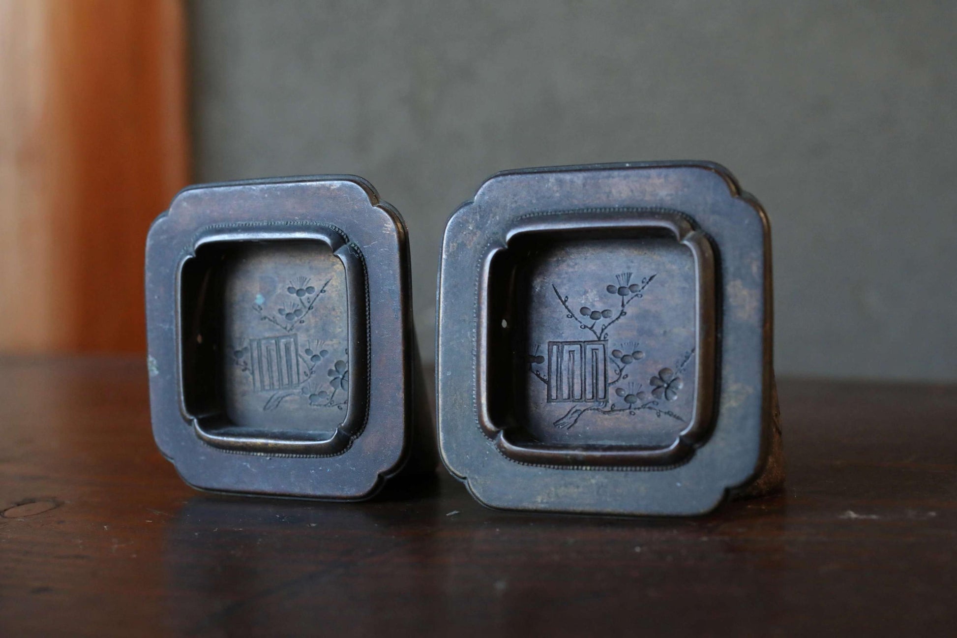 Two antique metal trinkets with intricate designs, placed on a wooden surface.