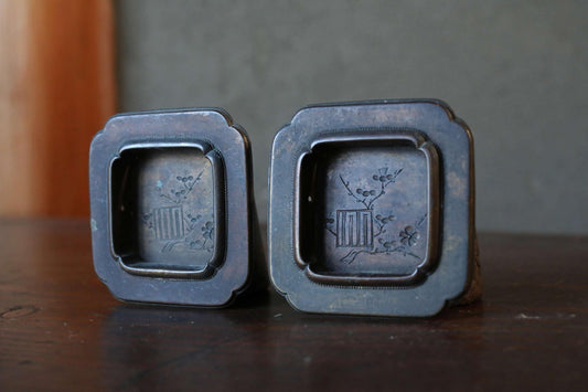 Two antique metal trinkets with intricate designs, placed on a wooden surface.