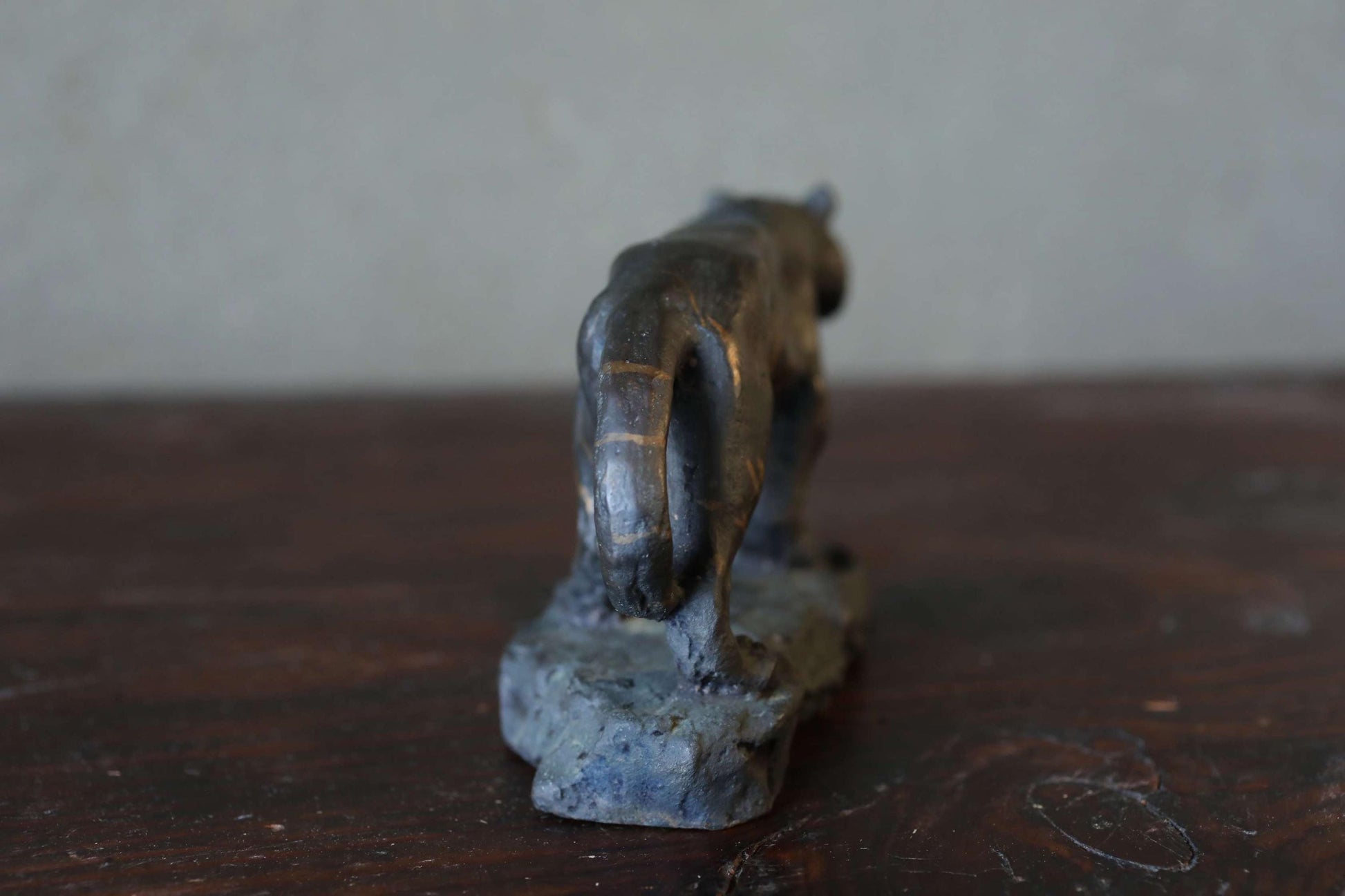 A small, dark-colored figurine of a cat or feline-like creature is sitting on a rock or stone base, positioned on a wooden surface.