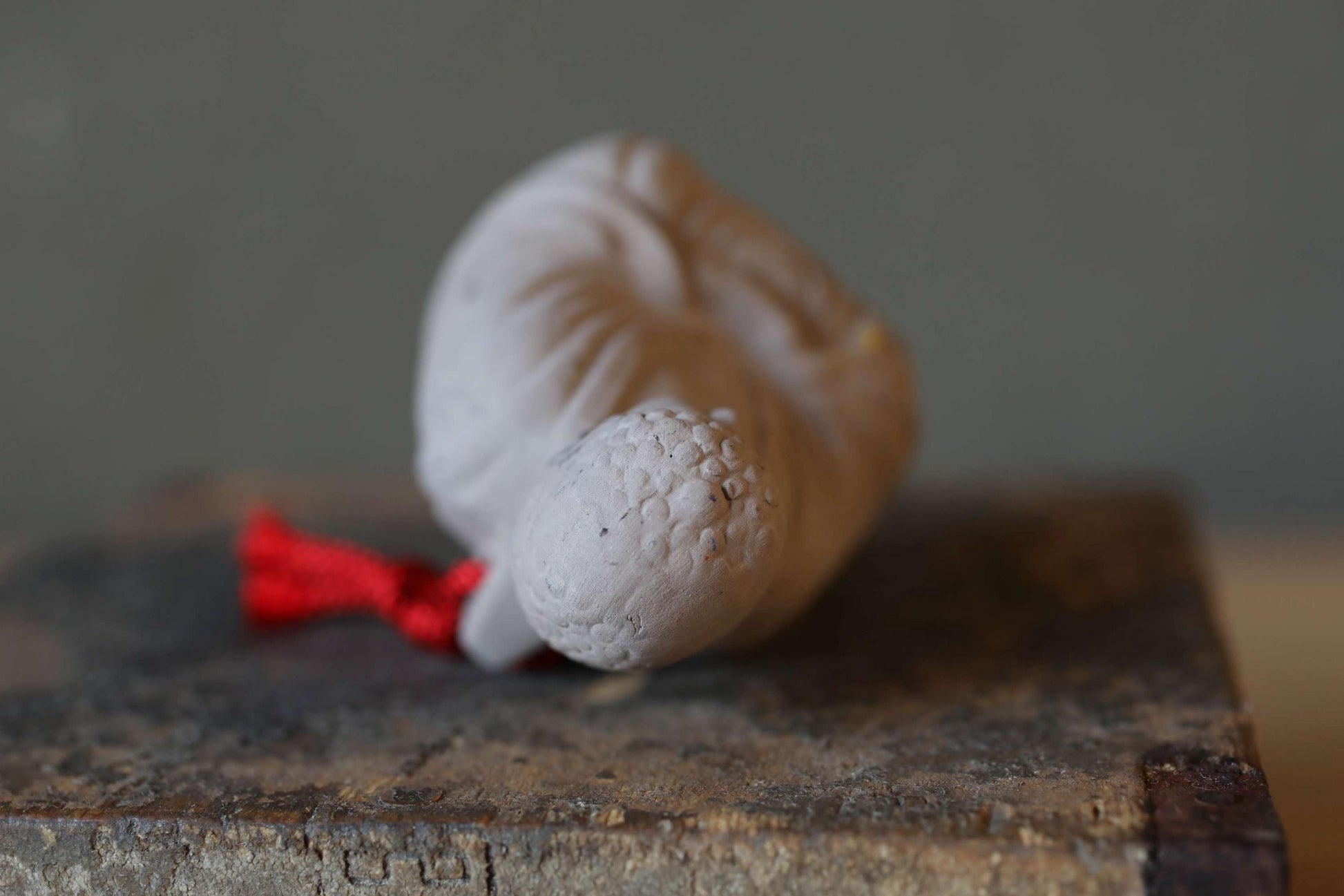A white ceramic object with a red ribbon tied around it, sitting on a wooden surface.