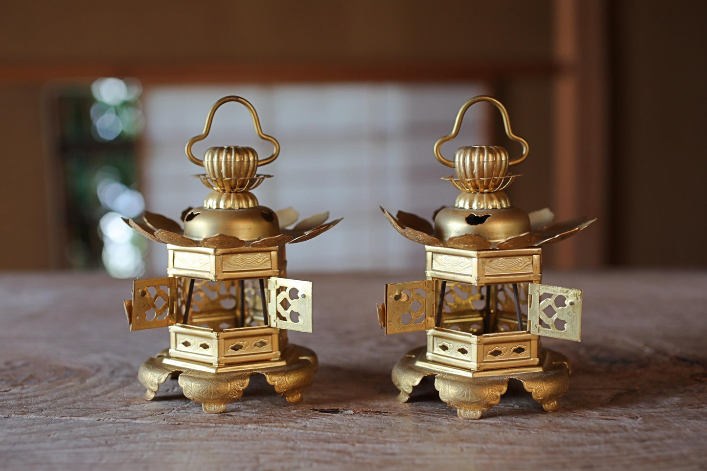 Two ornate golden lanterns with intricate designs are displayed on a wooden surface.