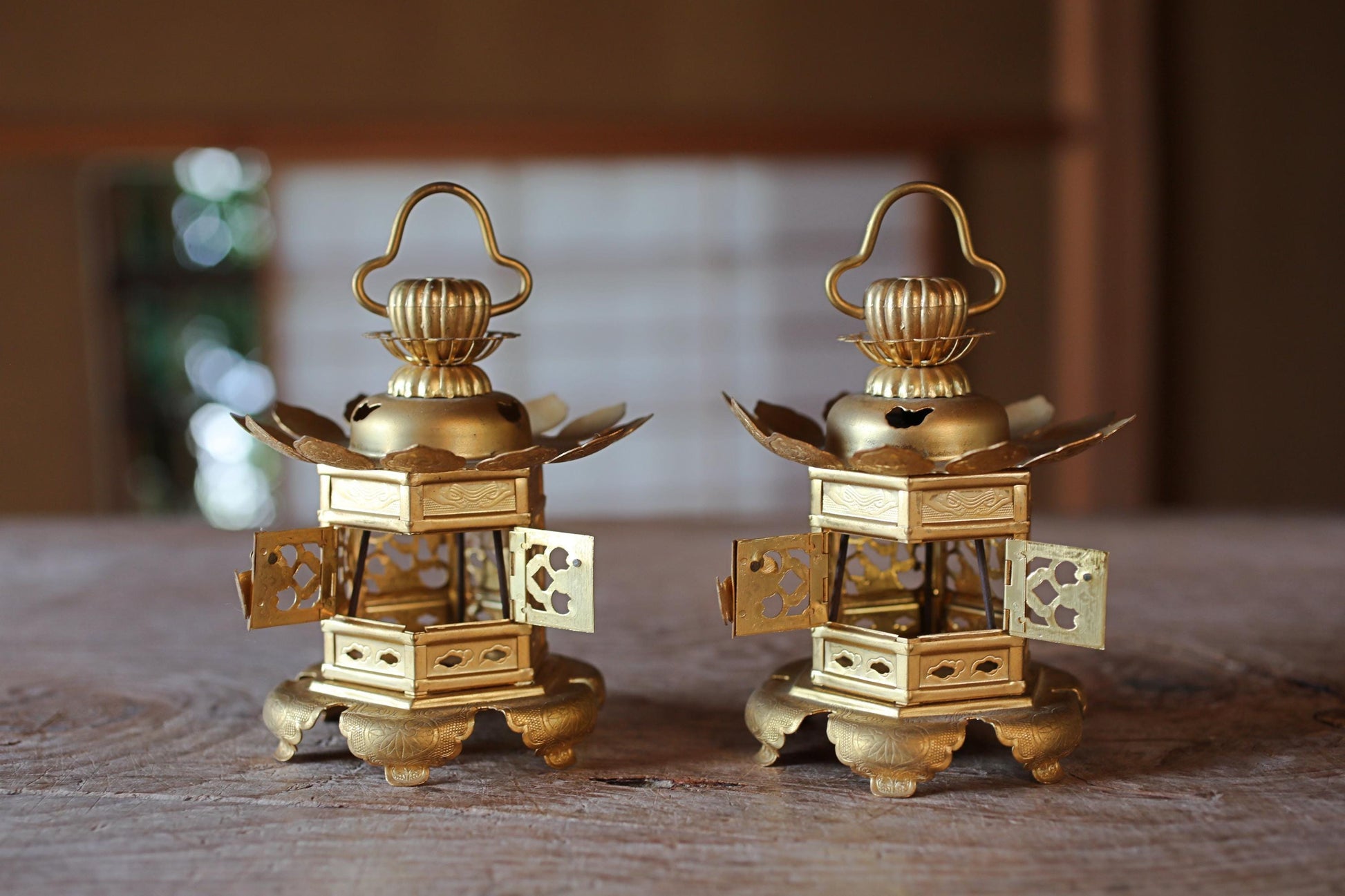 Two ornate golden lanterns with intricate designs are displayed on a wooden surface.