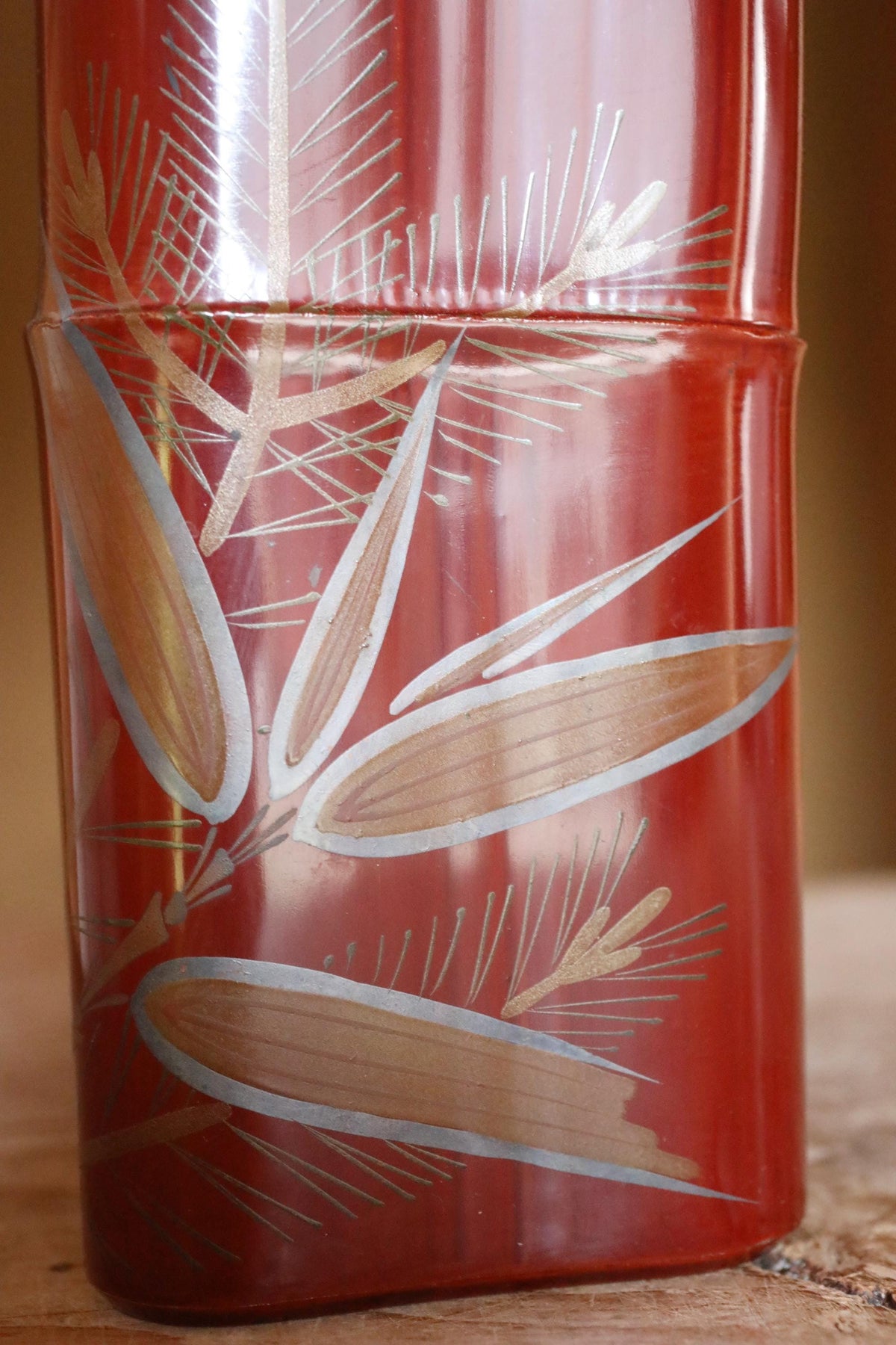 a red vase with a decorative design of leaves and branches on its surface.