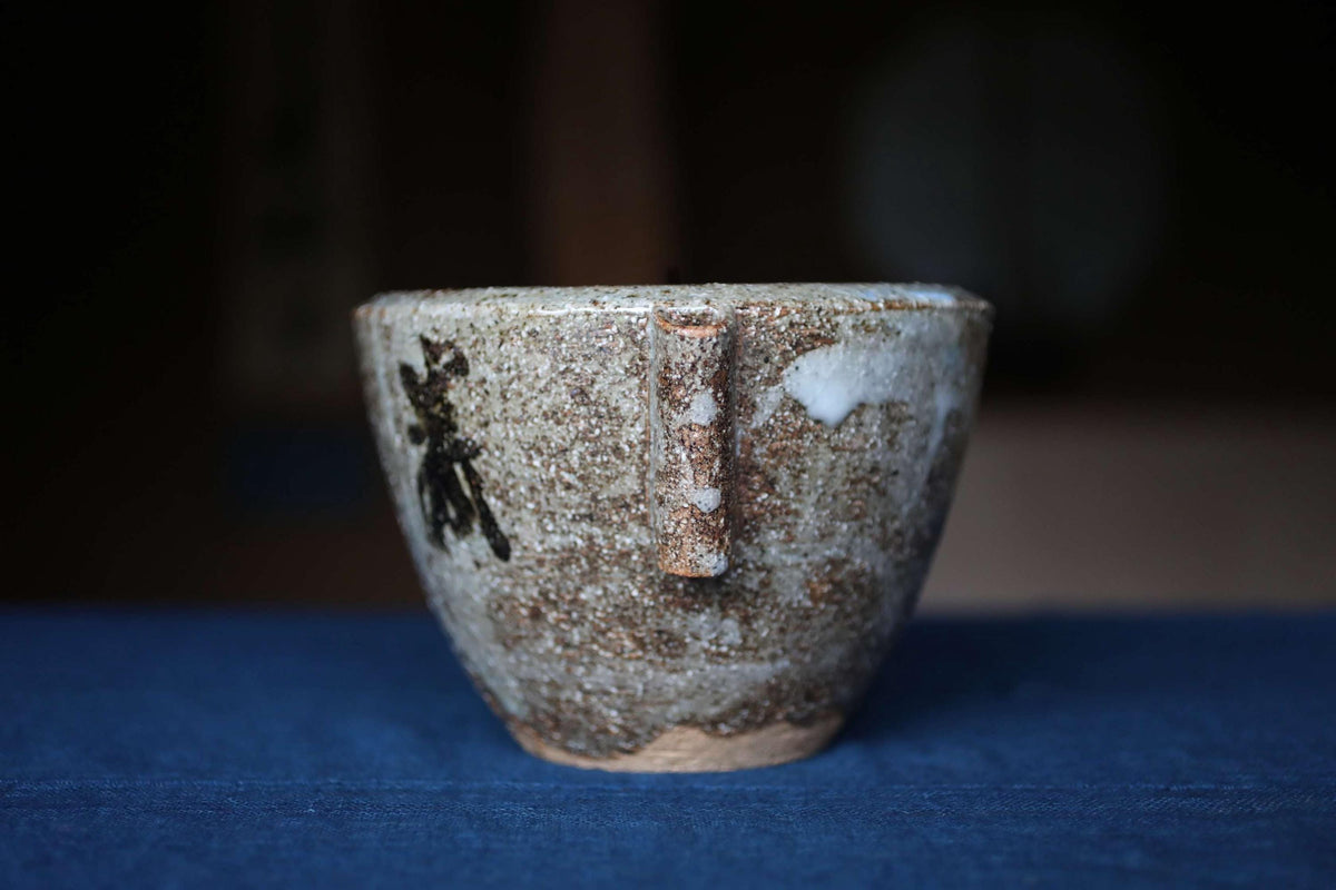 A ceramic mug with a textured surface and a handle, sitting on a blue surface.