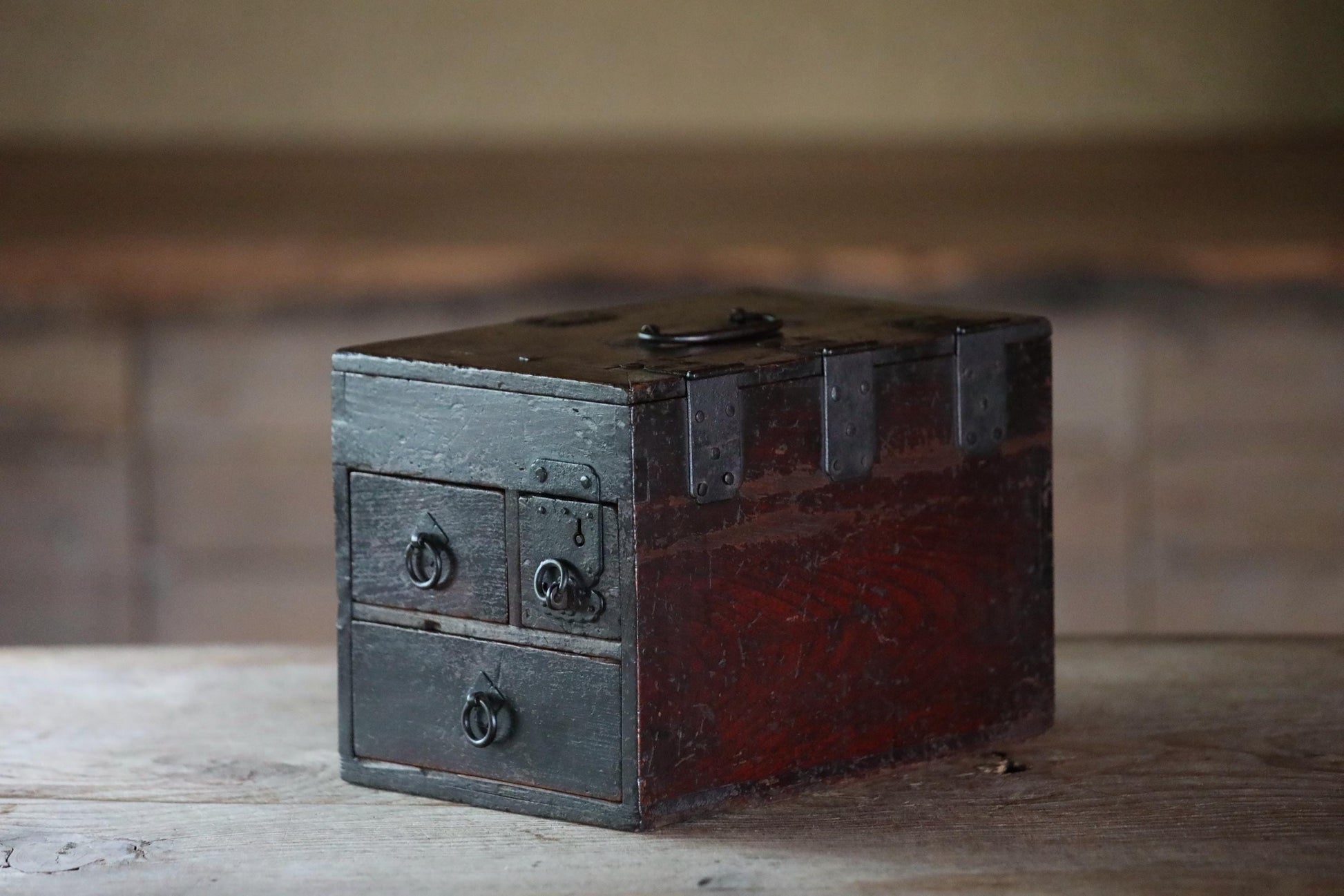 An old, weathered wooden chest with metal hardware sits on a wooden surface.