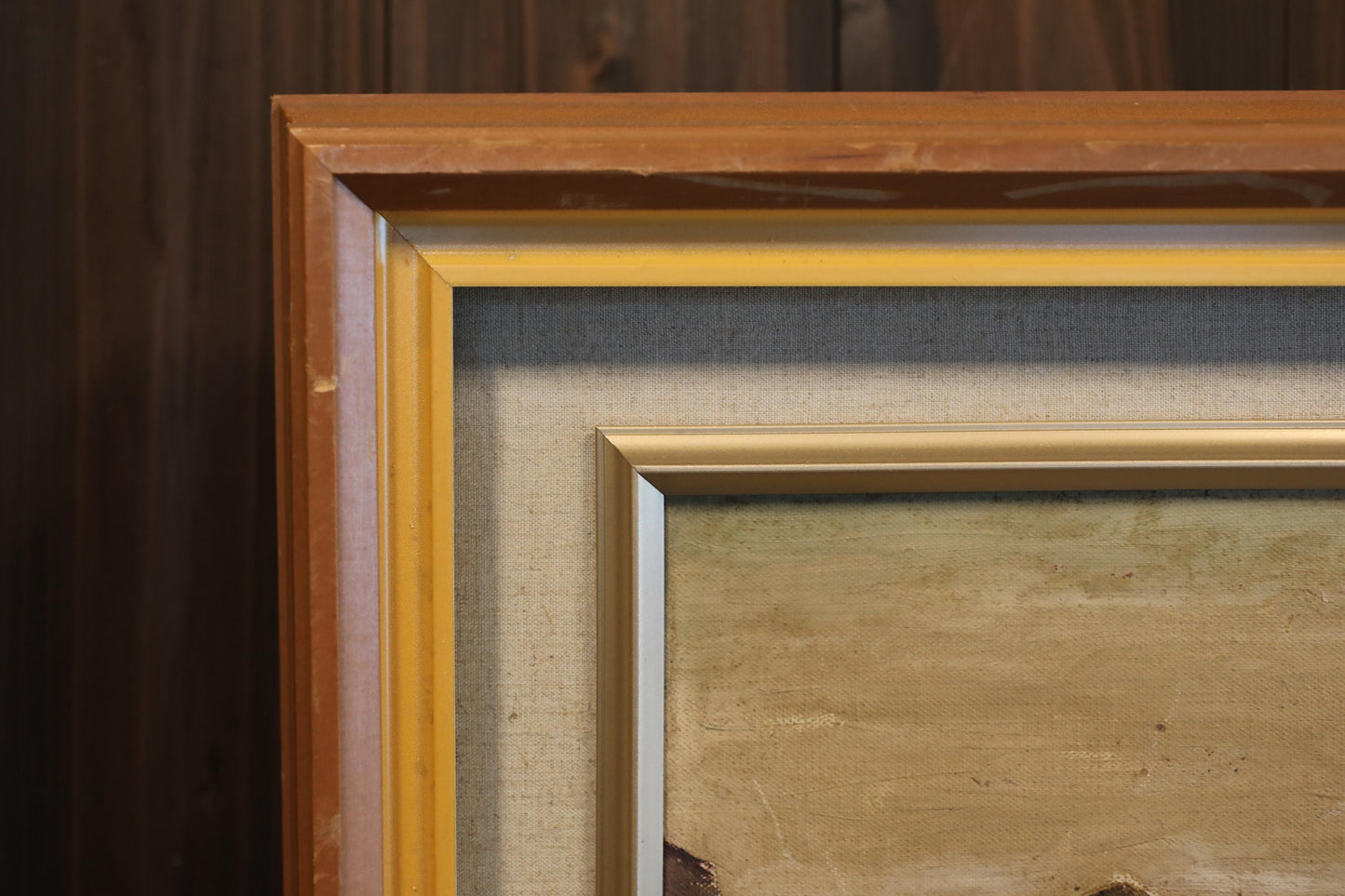 a close-up view of a framed painting with a wooden frame, set against a dark background.