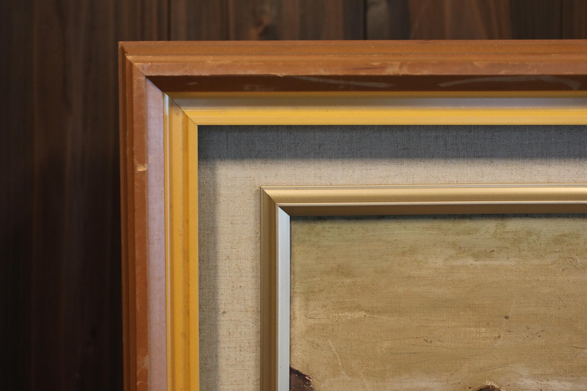 a close-up view of a framed painting with a wooden frame, set against a dark background.