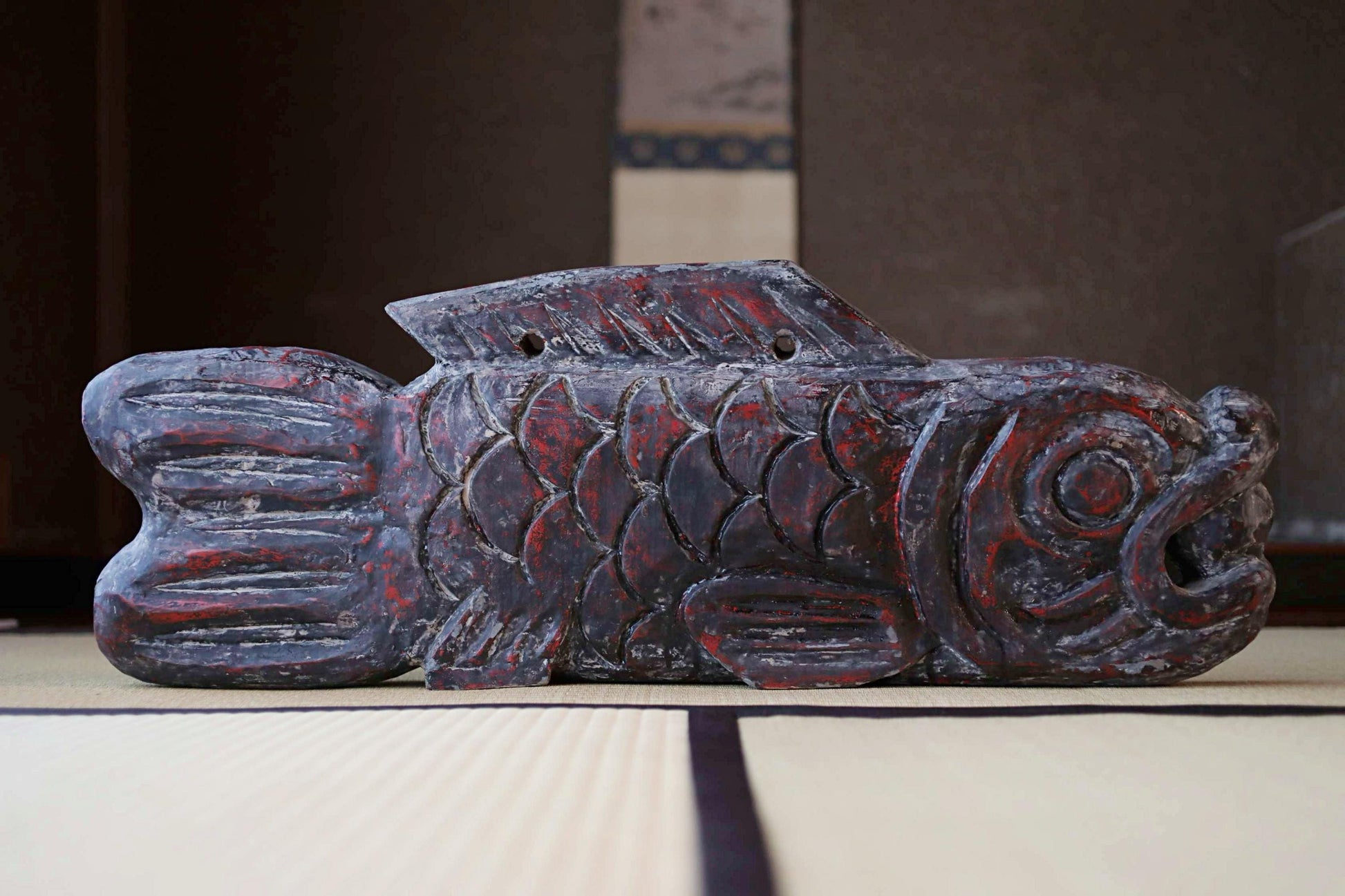 a wooden fish sculpture with a dark red and black color scheme, sitting on a white mat.