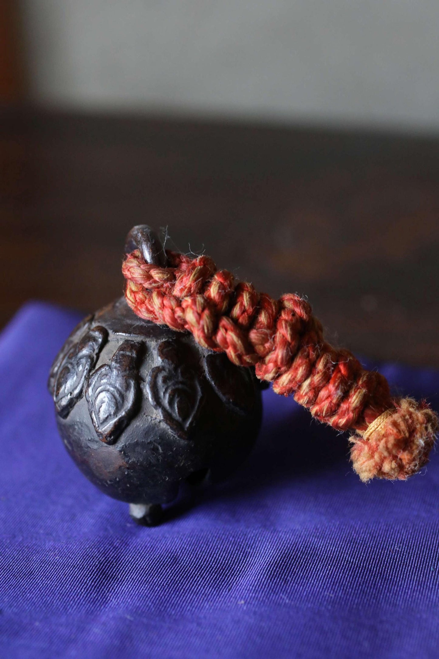 A black metal bell with a red rope or cord wrapped around it, resting on a blue fabric surface.