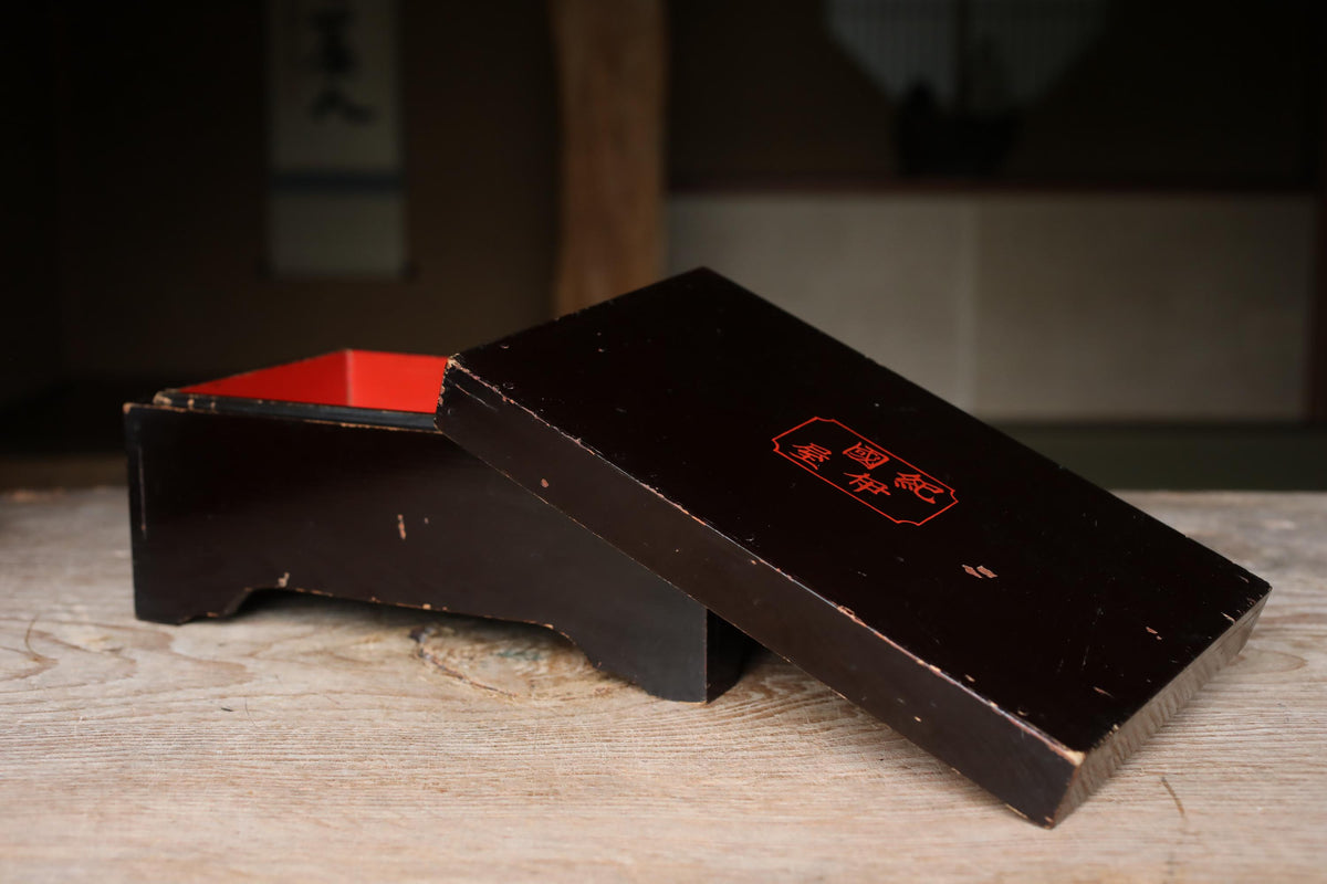 An old, black wooden box with a red interior, placed on a wooden surface.