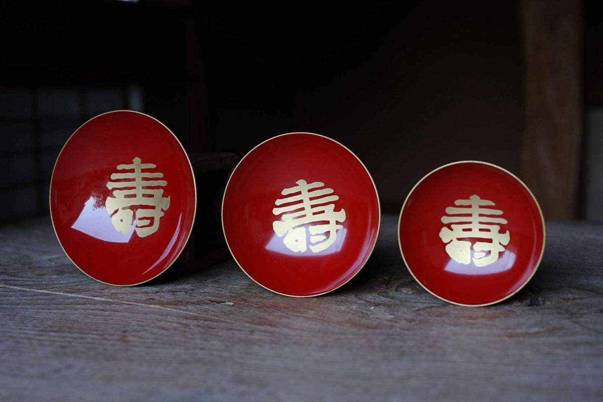 Three red plates with gold Chinese characters are arranged on a wooden surface.