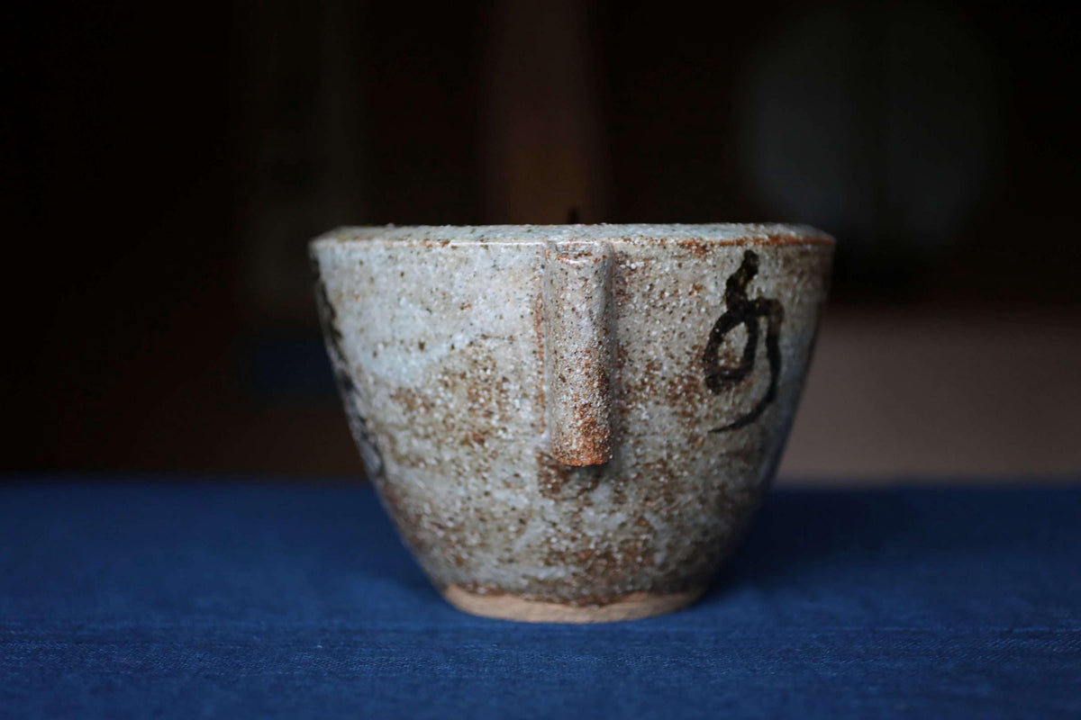 A ceramic mug with a textured surface and a black symbol on it, placed on a blue surface.