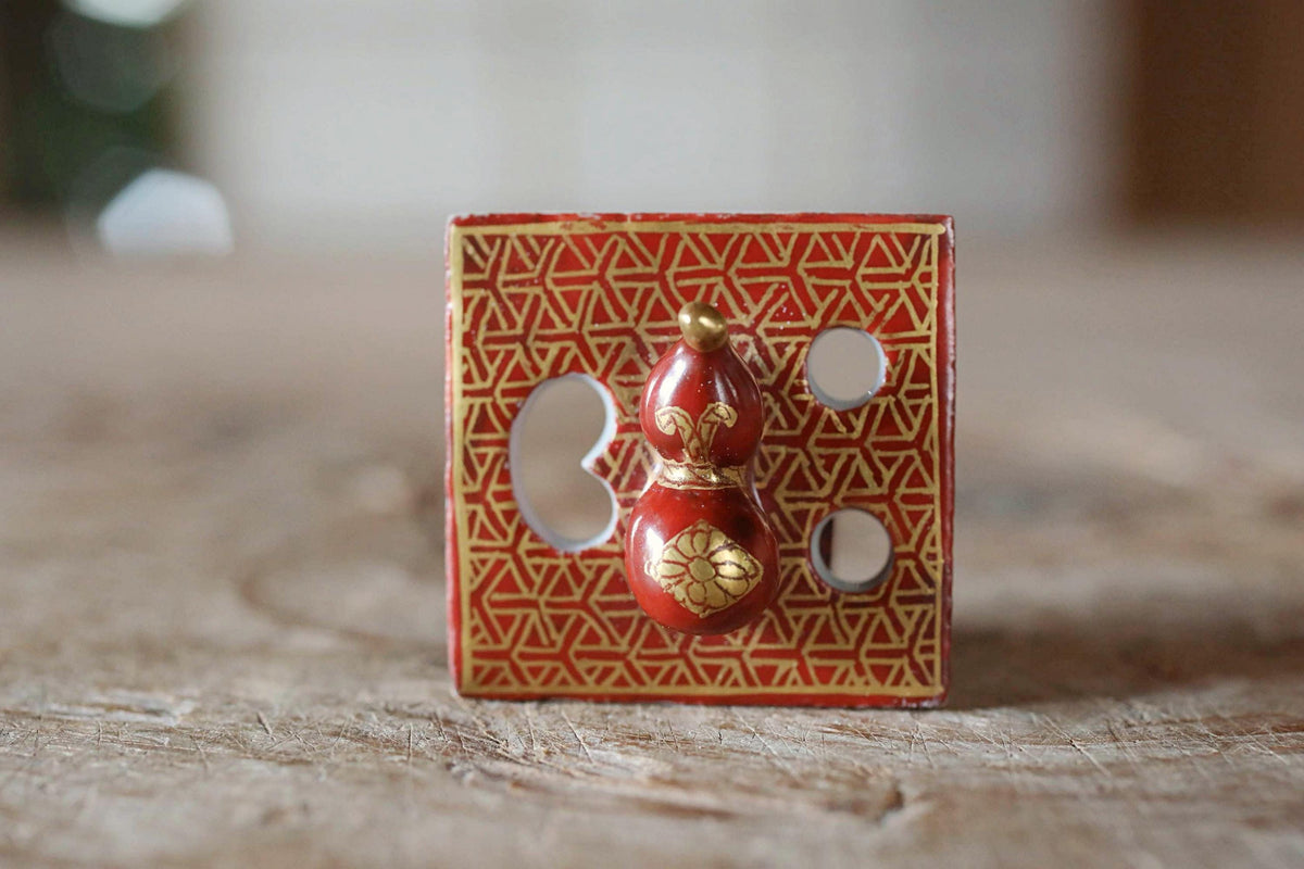 A red and gold decorative object with a floral design, placed on a wooden surface.