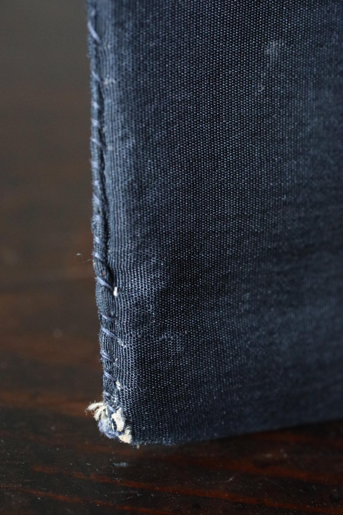 A close-up view of a dark blue fabric, possibly denim, with visible stitching and a slightly worn appearance.