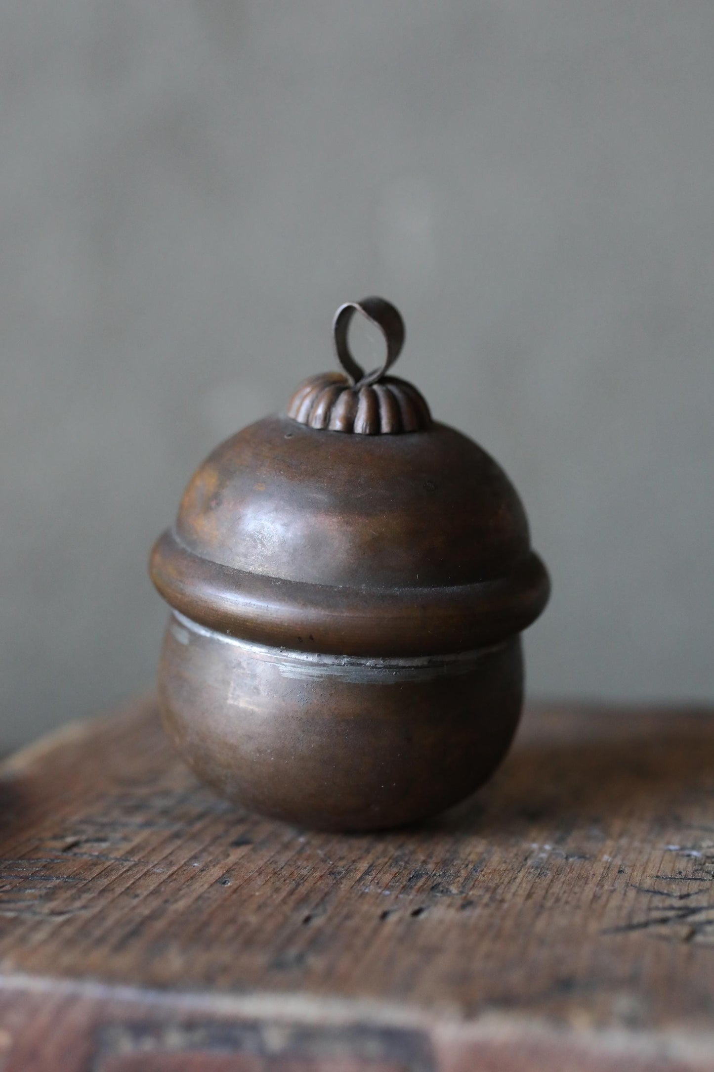 A round, metal container with a decorative top sits on a wooden surface.