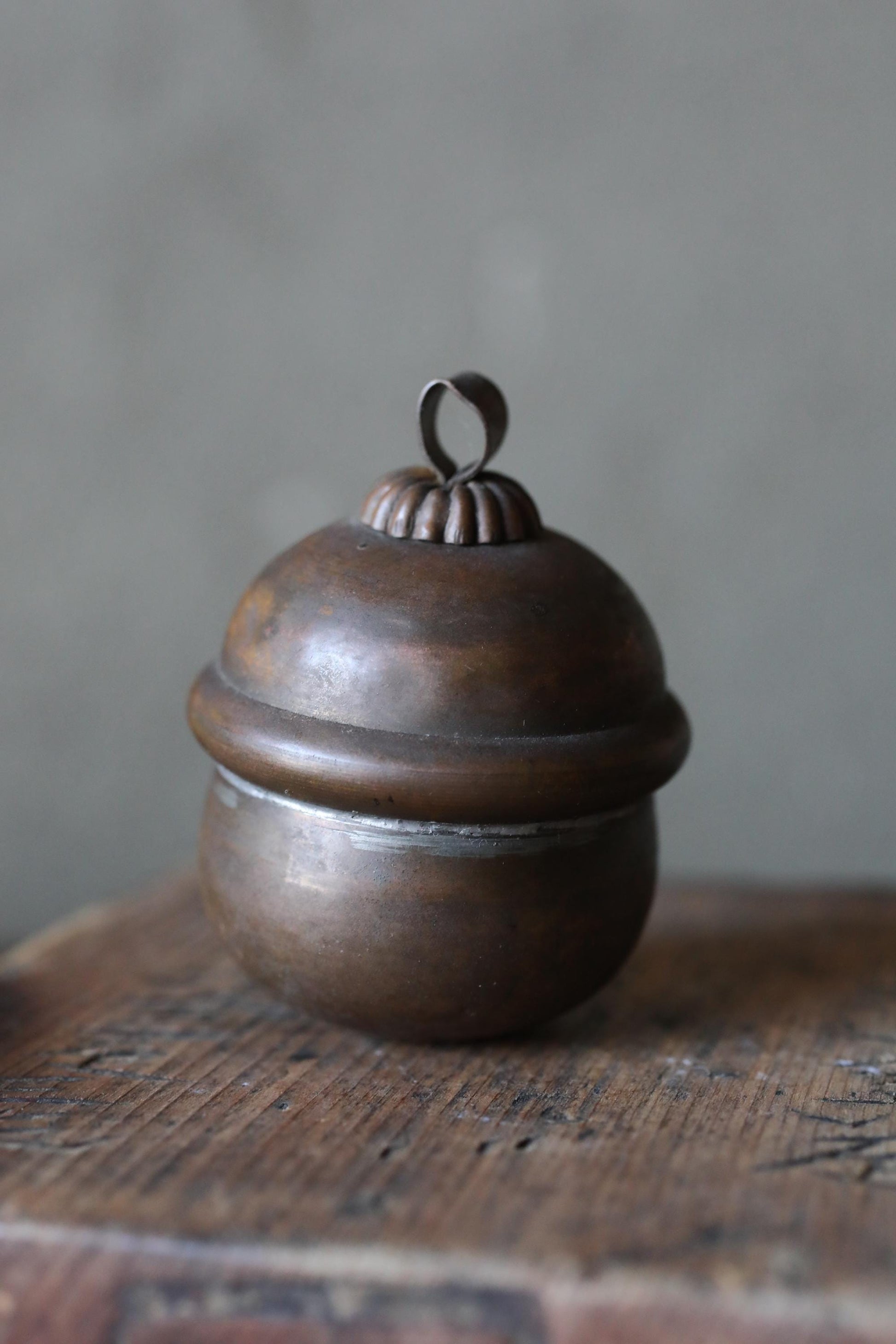 A round, metal container with a decorative top sits on a wooden surface.