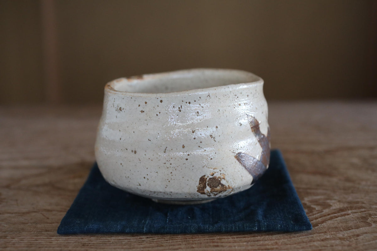 A white ceramic bowl with brown speckles sits on a blue cloth on a wooden surface.