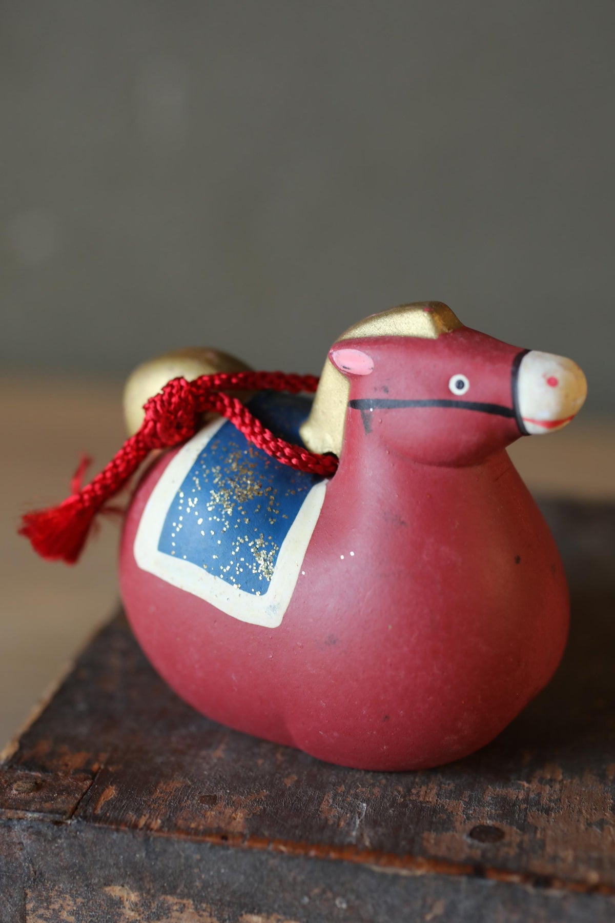 A red ceramic cow figurine with a blue and gold design, sitting on a wooden surface.