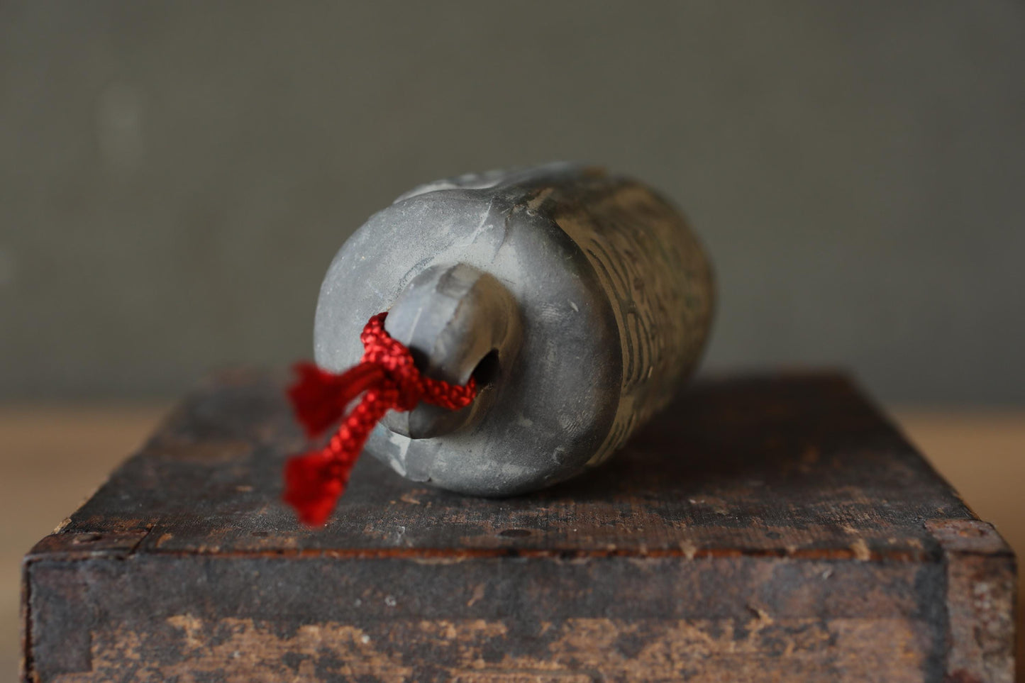 A gray metal object with a red string tied around it, resting on a wooden surface.
