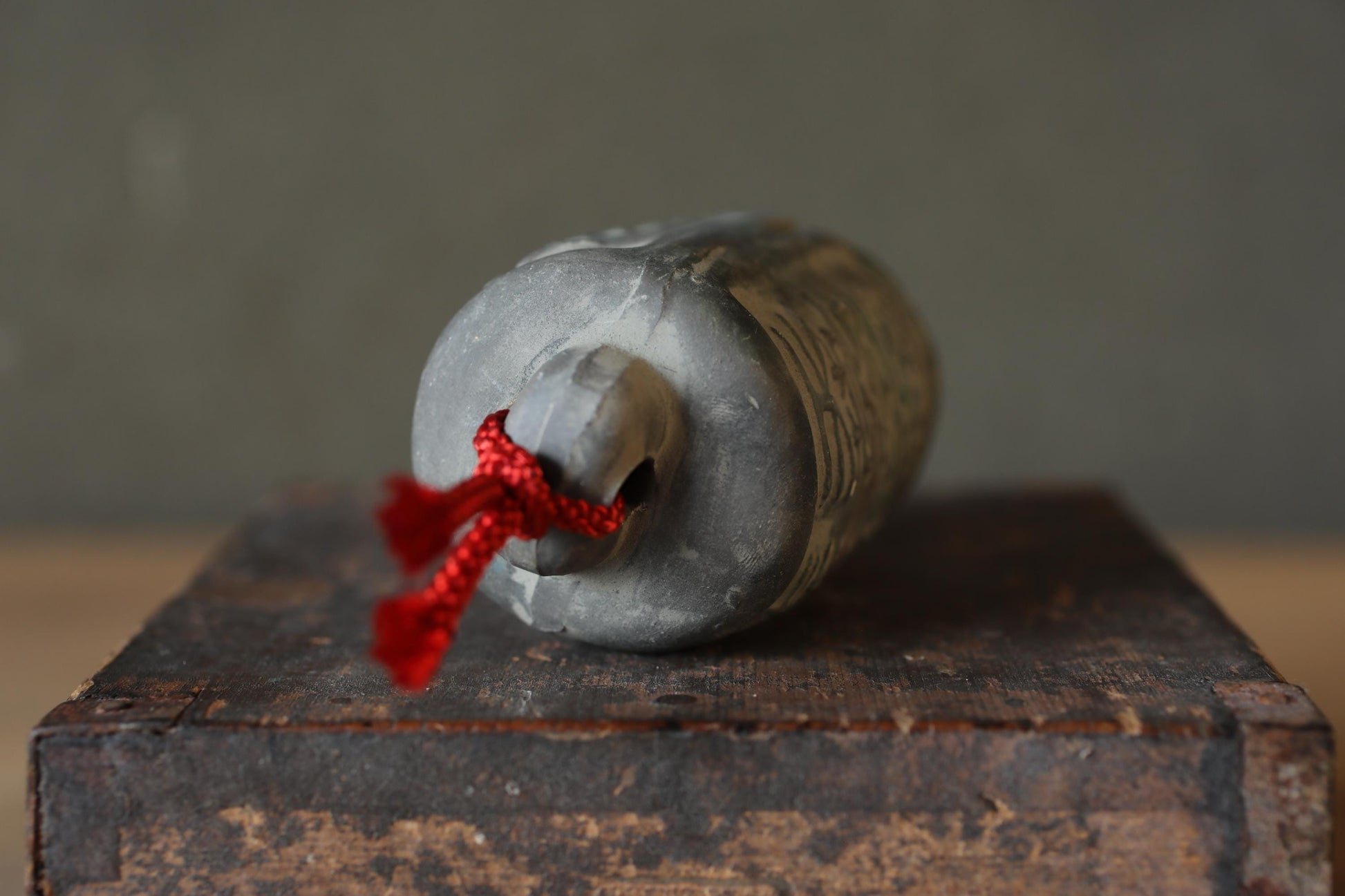 A gray metal object with a red string tied around it, resting on a wooden surface.