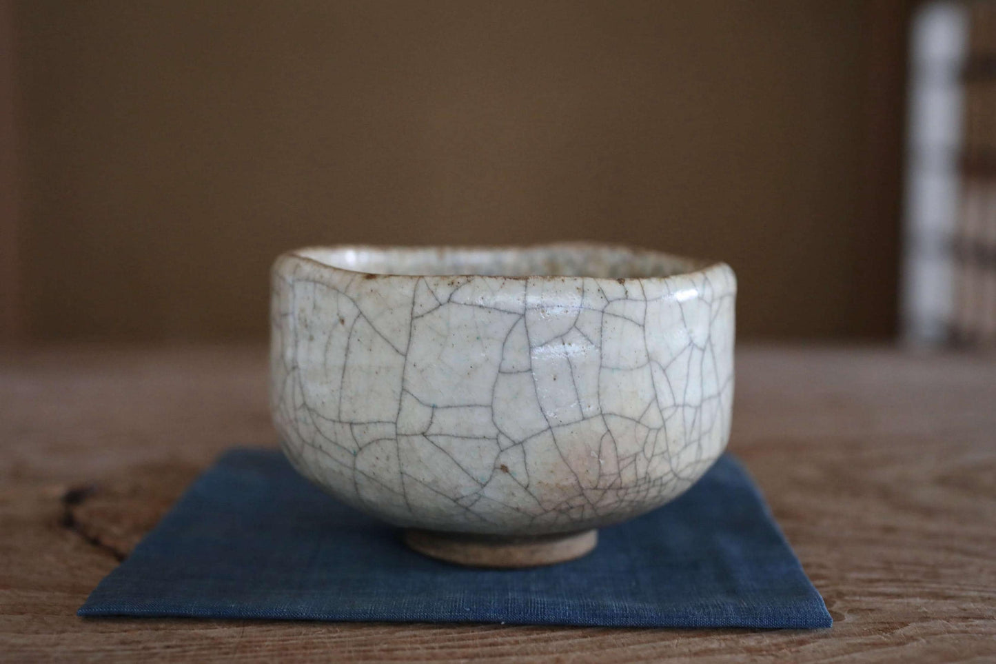 A white ceramic bowl with a cracked and textured surface sits on a blue cloth on a wooden surface.