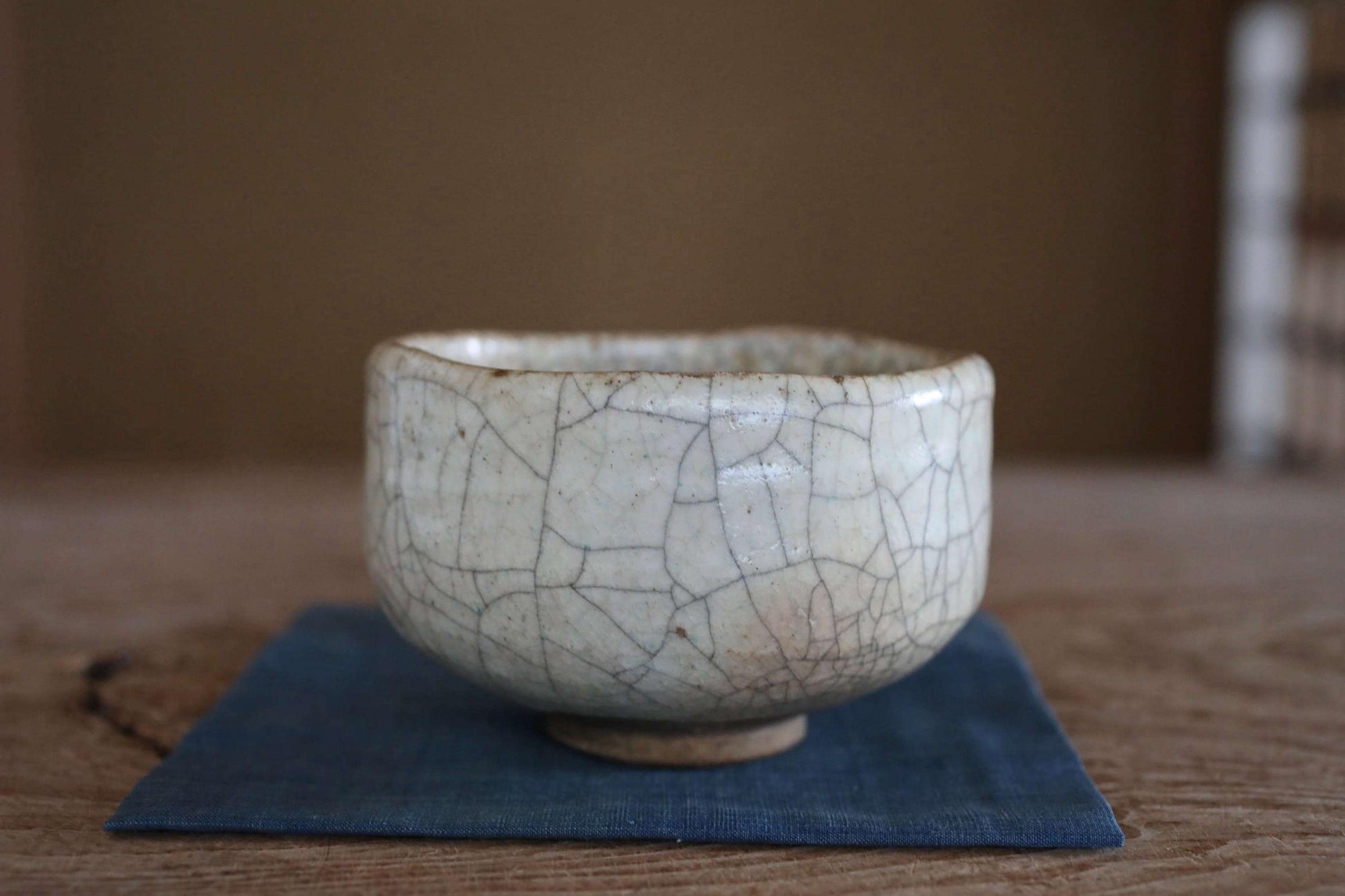 A white ceramic bowl with a cracked and textured surface sits on a blue cloth on a wooden surface.