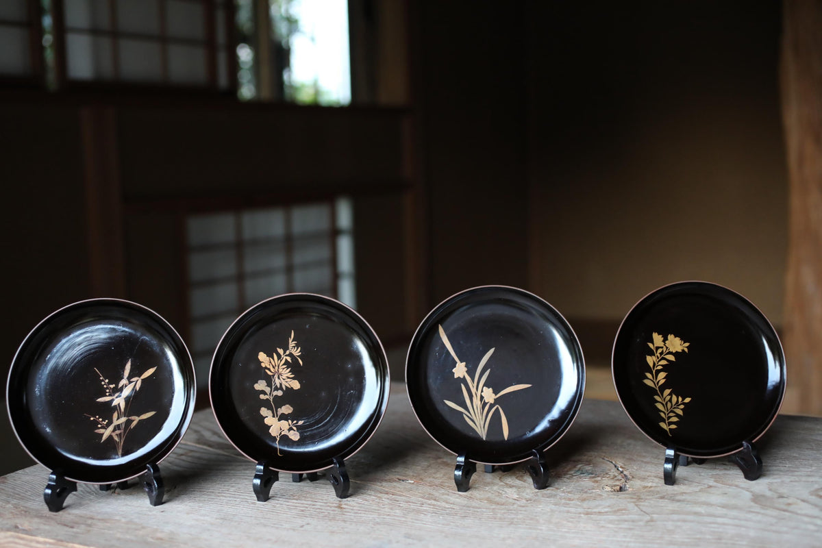 A row of four black plates with gold floral designs, each placed on a stand.