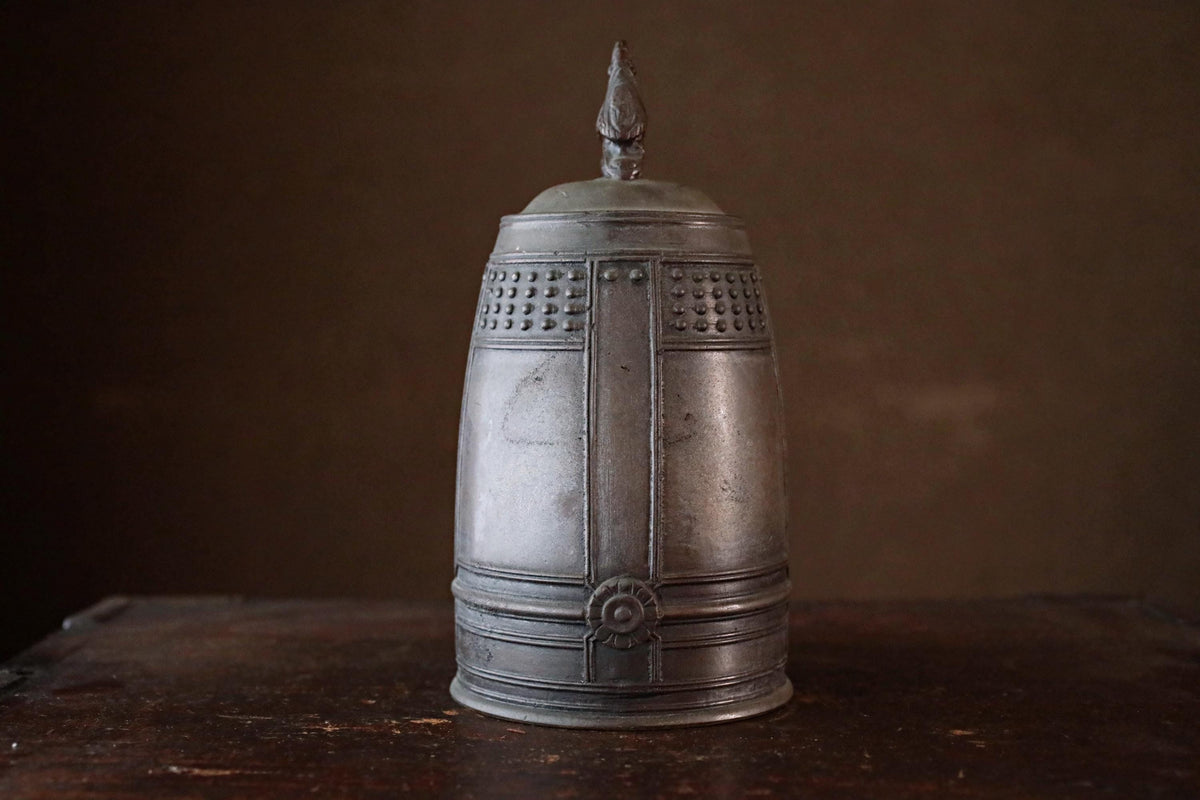 A metal container with a decorative top sits on a wooden surface against a dark background.
