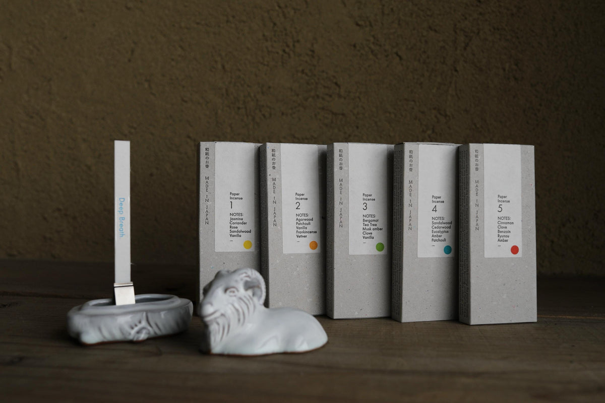 a collection of five white boxes with black text, arranged in a row on a wooden surface. There is also a small white ceramic figurine of a ram in the foreground.