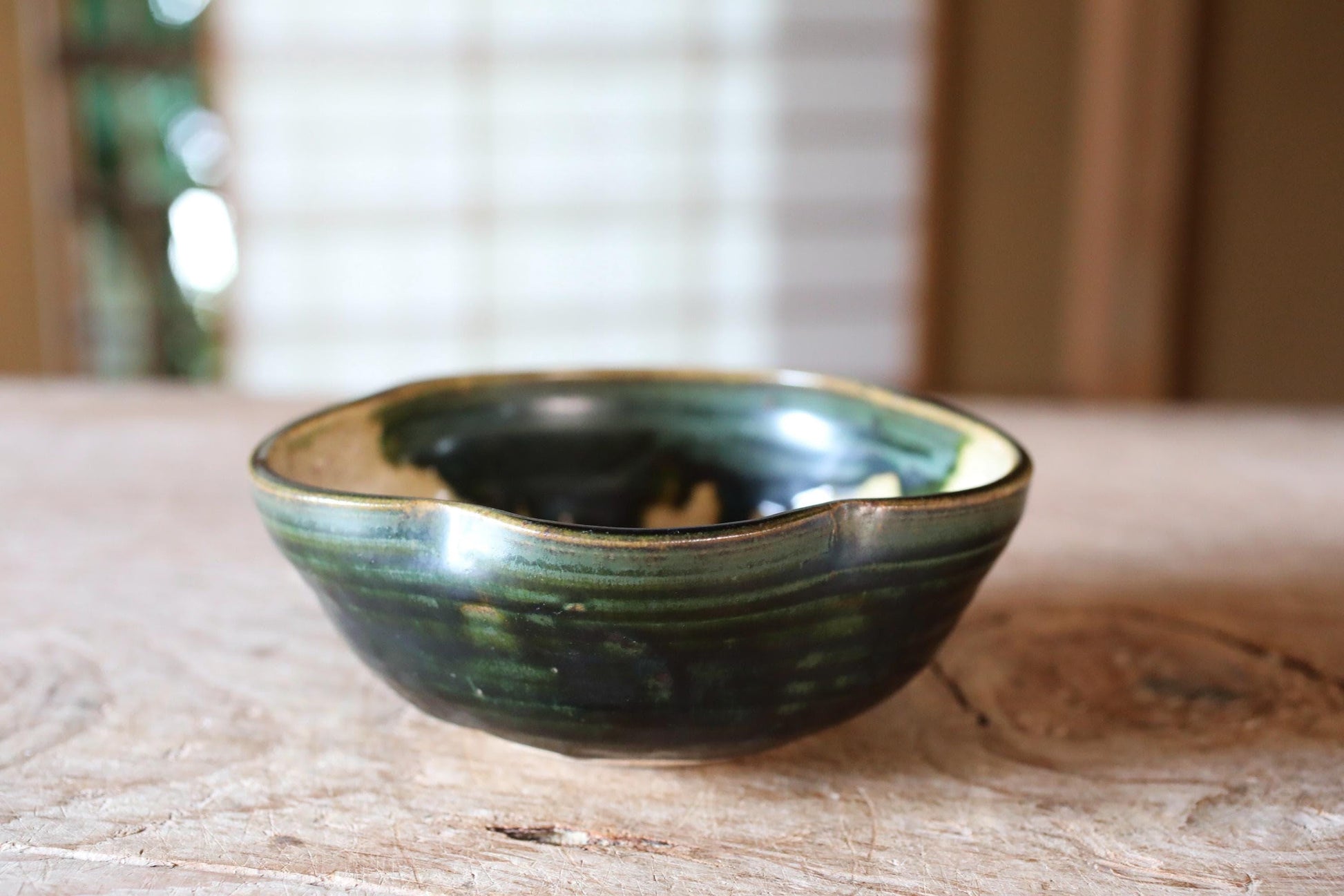 A ceramic bowl with a green and black glaze sits on a wooden surface.